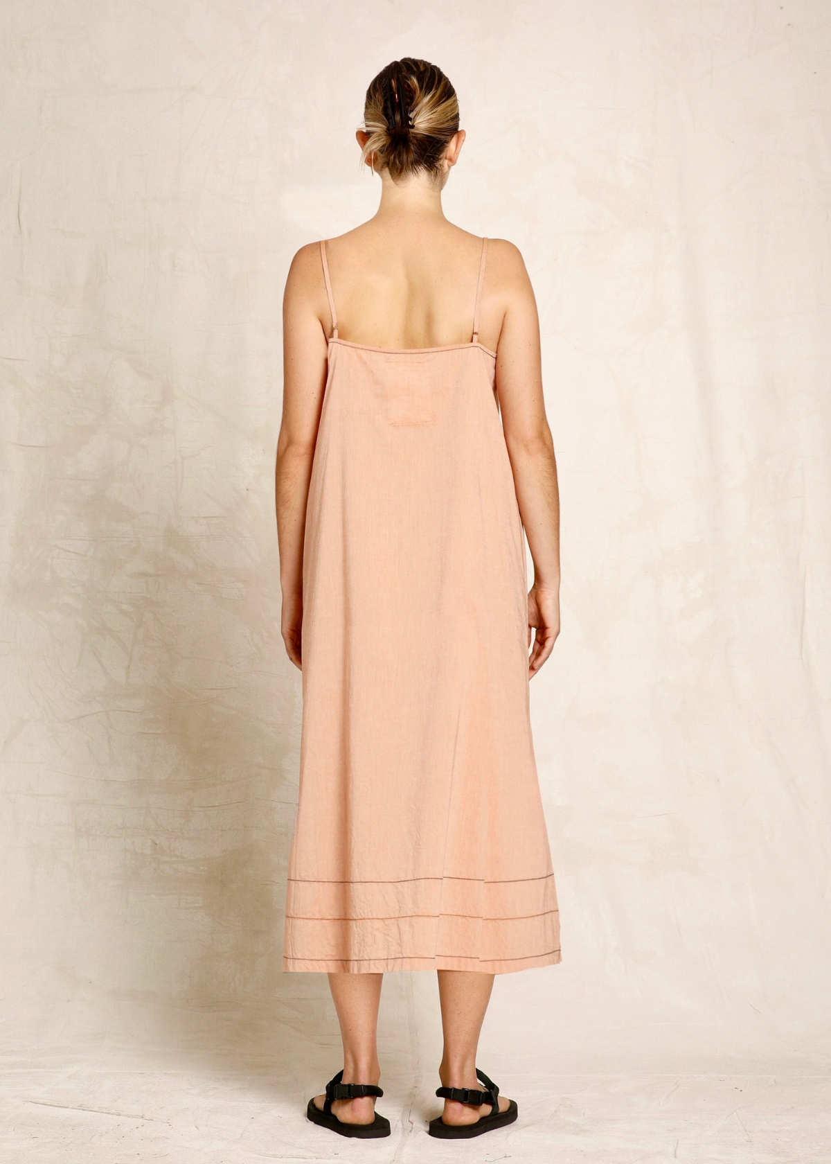 rear view of Woman wearing a light pink dress with thin straps on a plain background