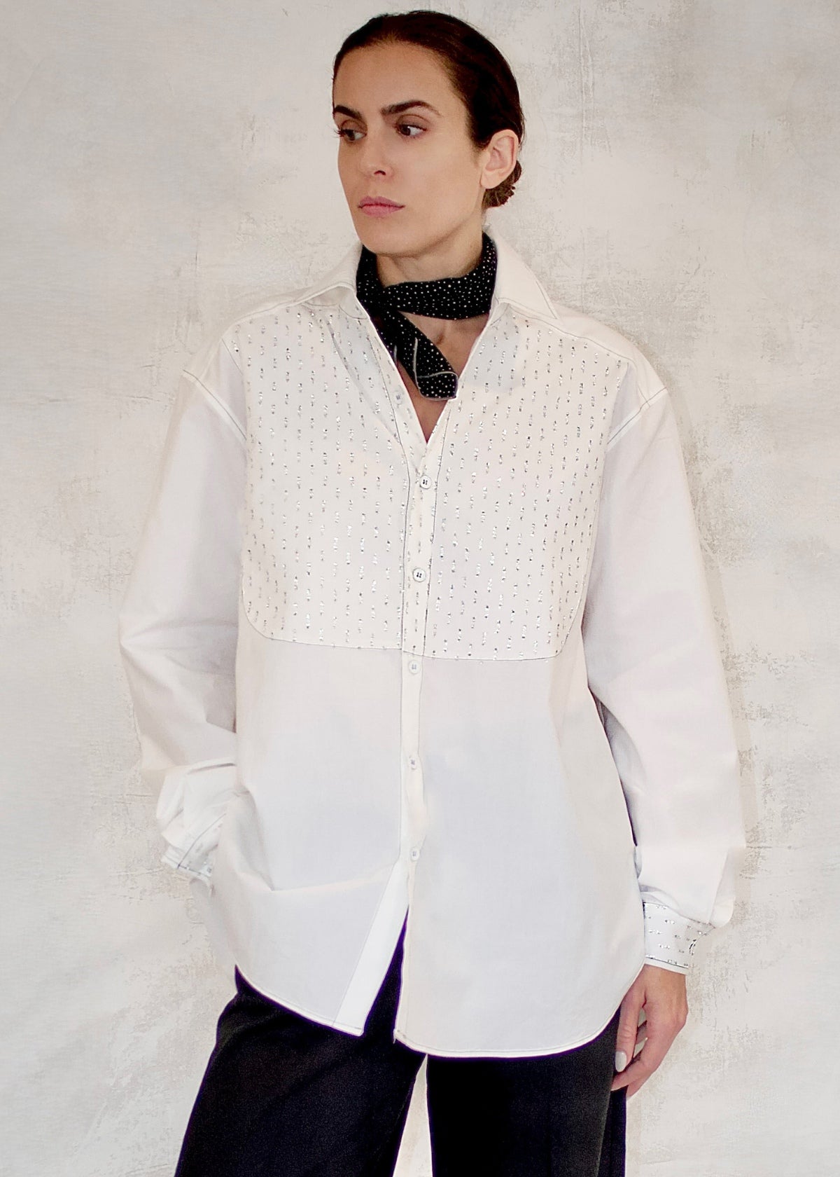 Person wearing a white blouse with silver metalic details against a plain background