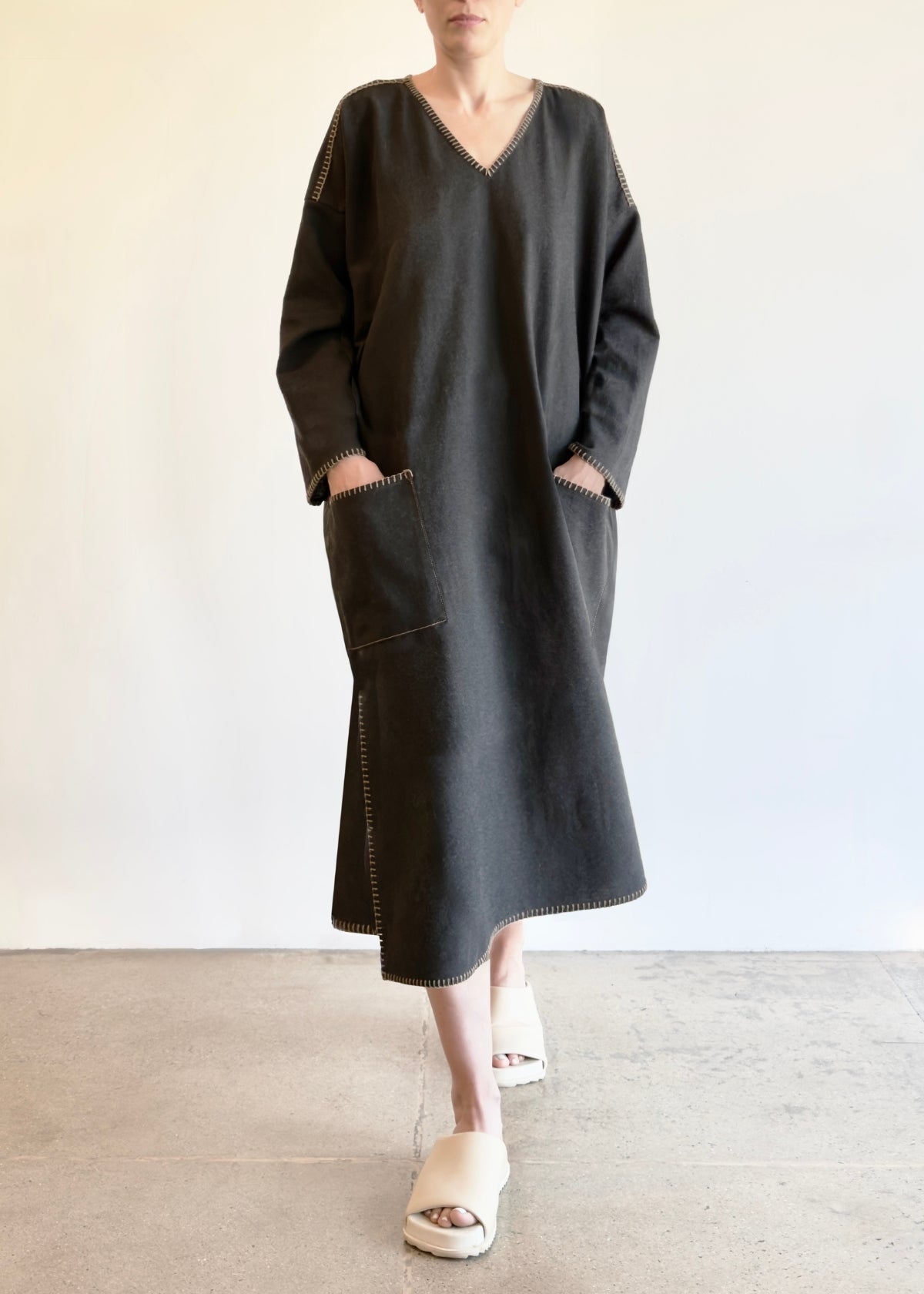 Person wearing a dark gray dress with hands in pockets against a plain background