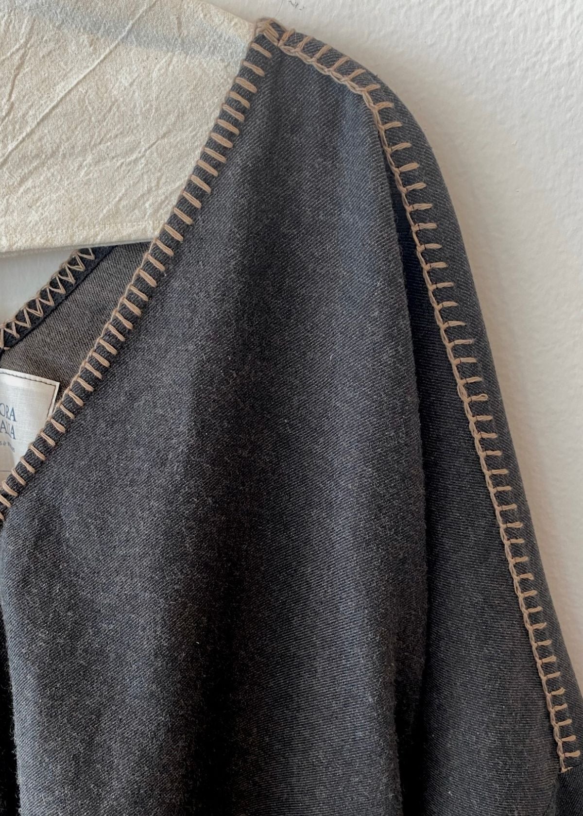 Shoulder-v-neck of dark gray top with light brown stitching on a textured white background