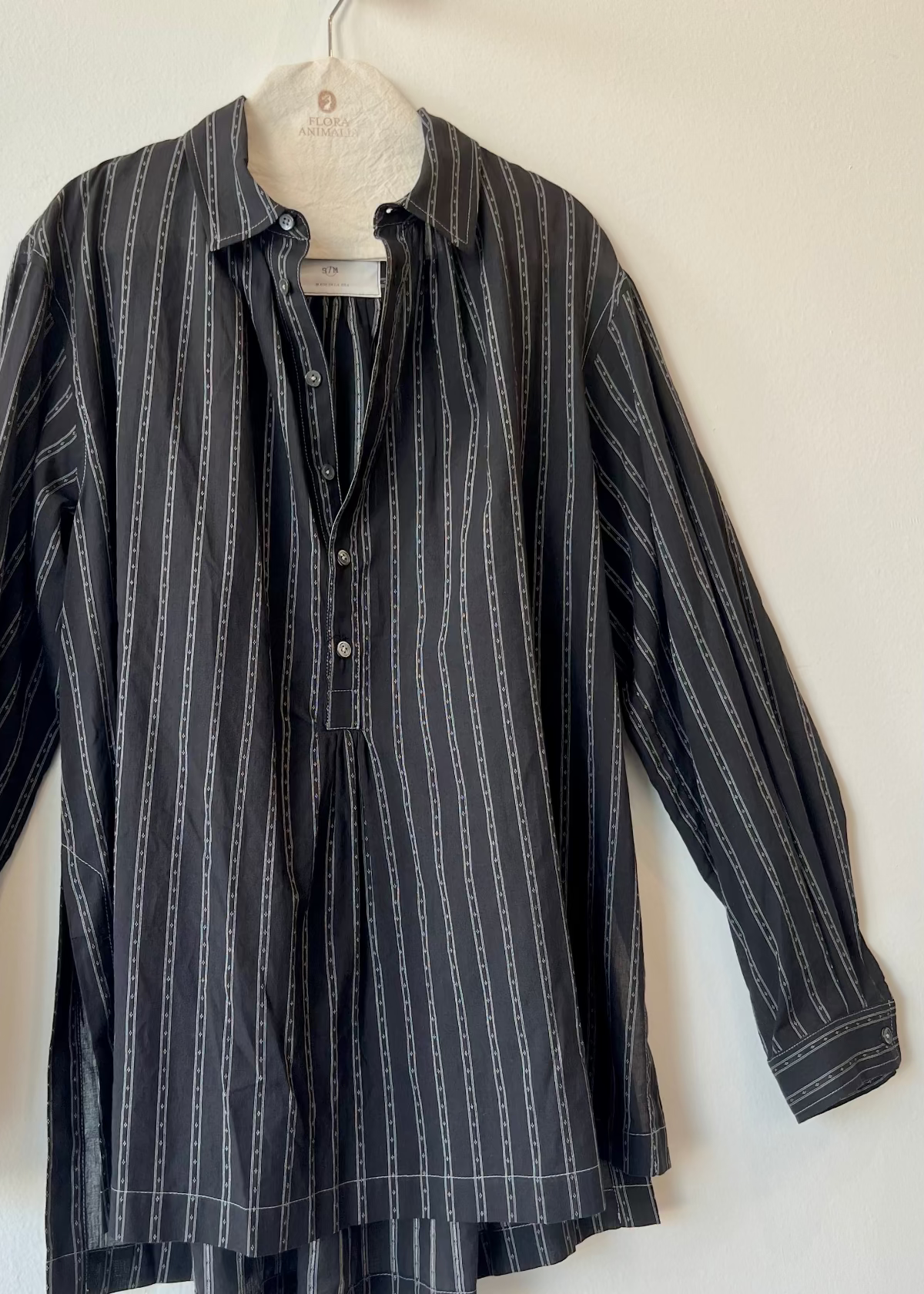 black shirt with white stripes and unbuttoned collar hanging against white wall