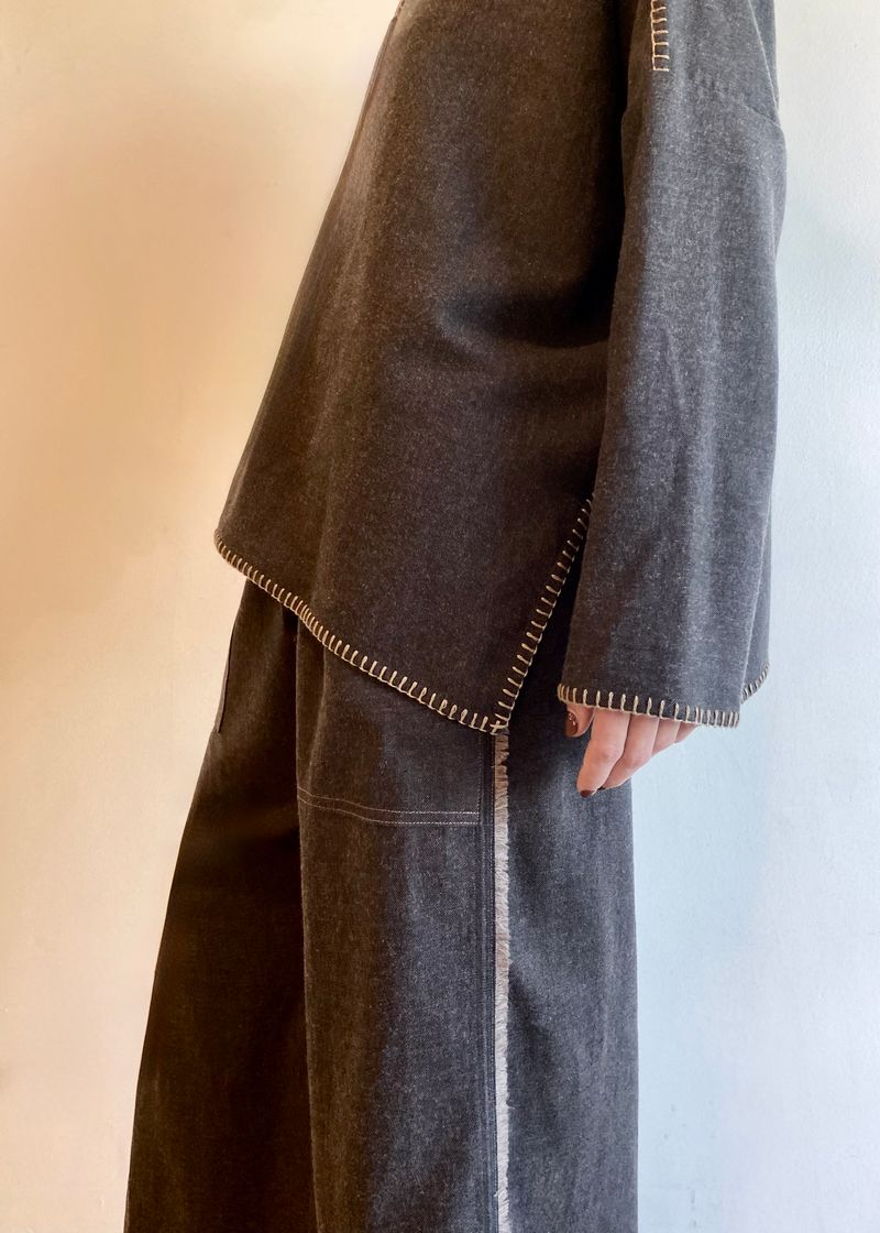side view of blanket stitch edge detail on Person wearing a gray poncho shirt and gray pants standing against a plain background