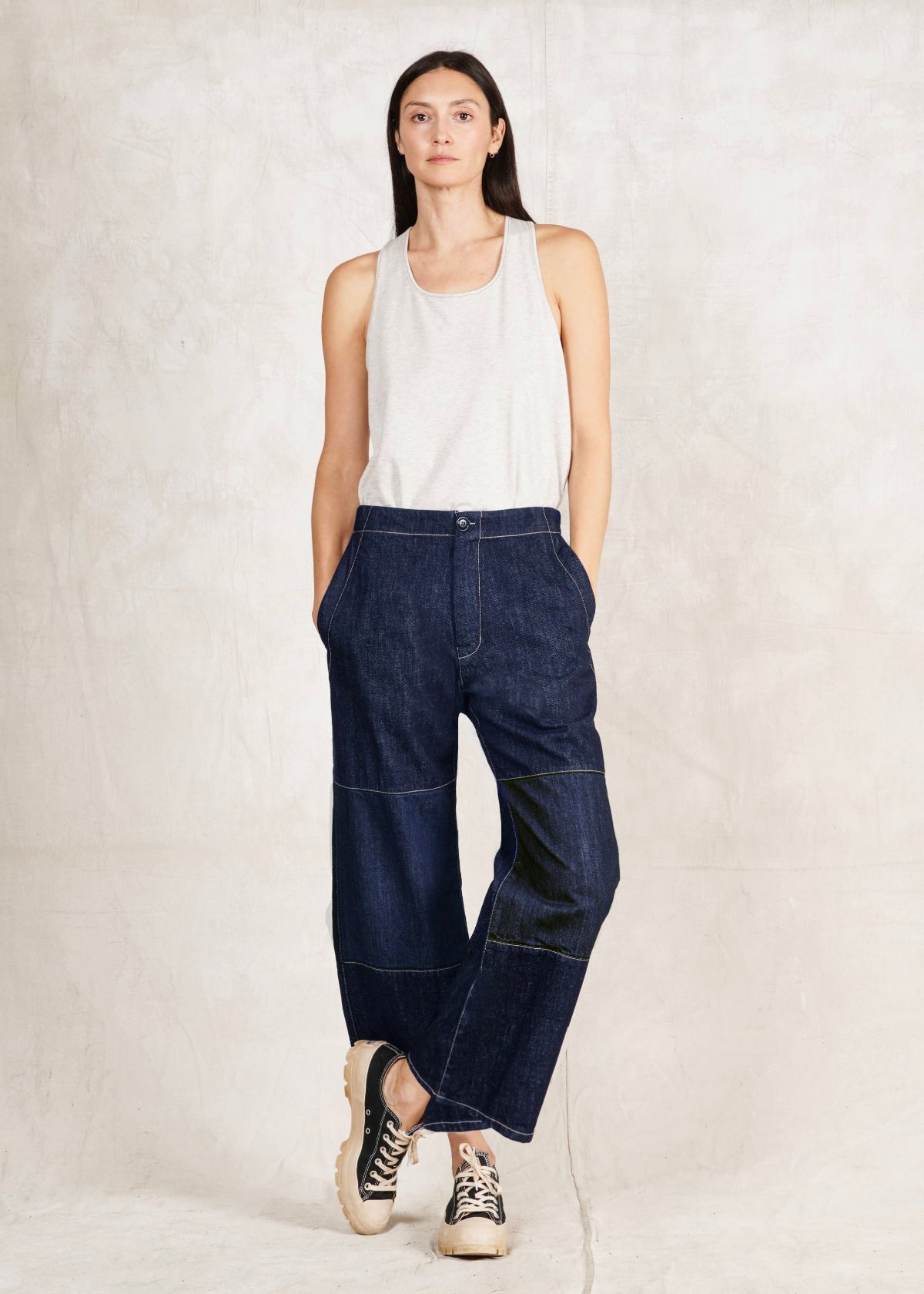 Woman wearing dark blue jeans and a white top against a plain background
