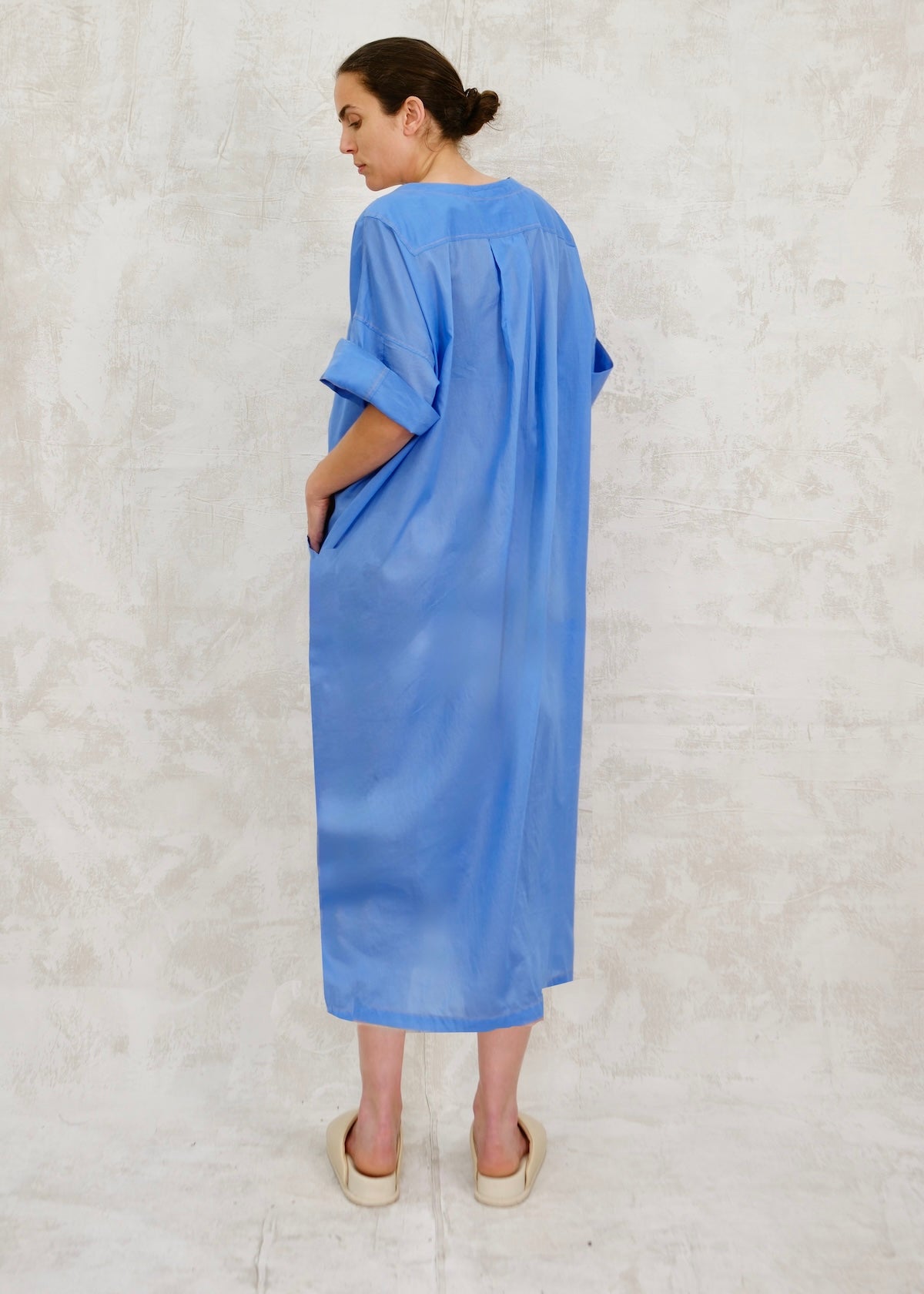Woman looking over her shoulder wearing a blue dress against a light gray background
