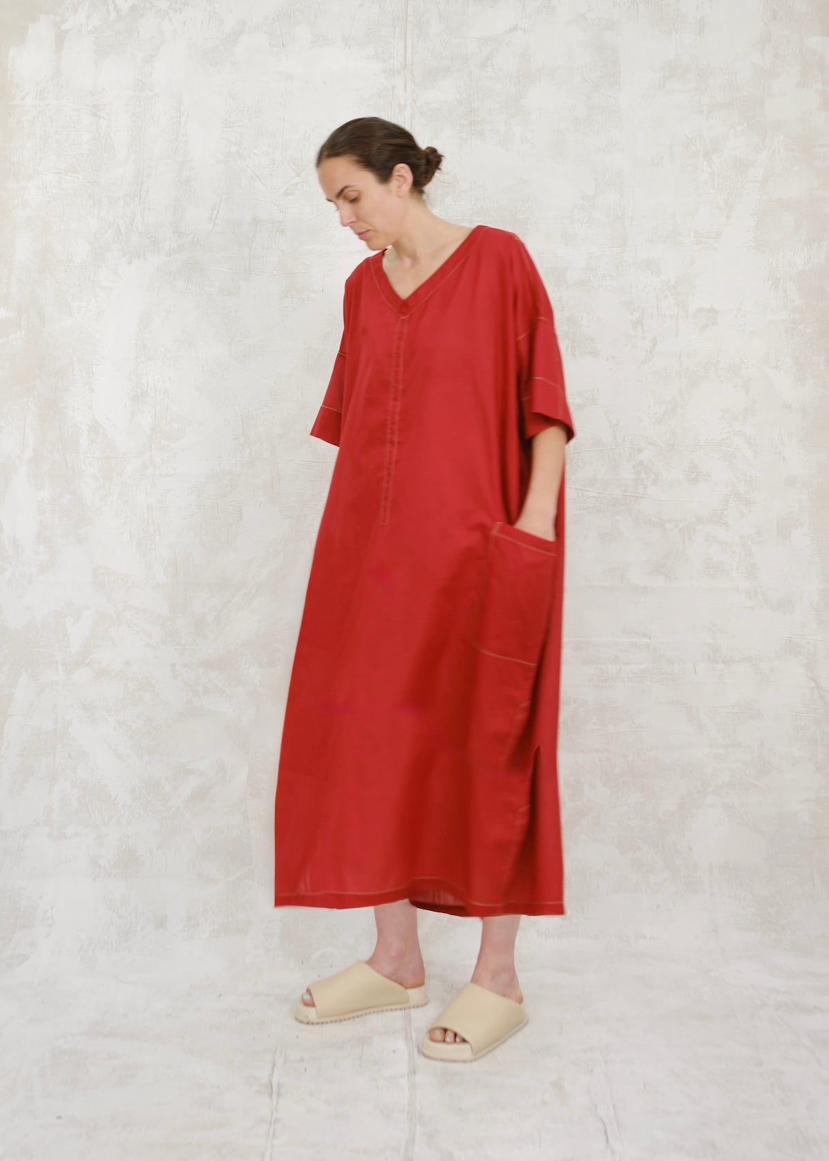 Woman wearing a red dress standing against a textured white wall.