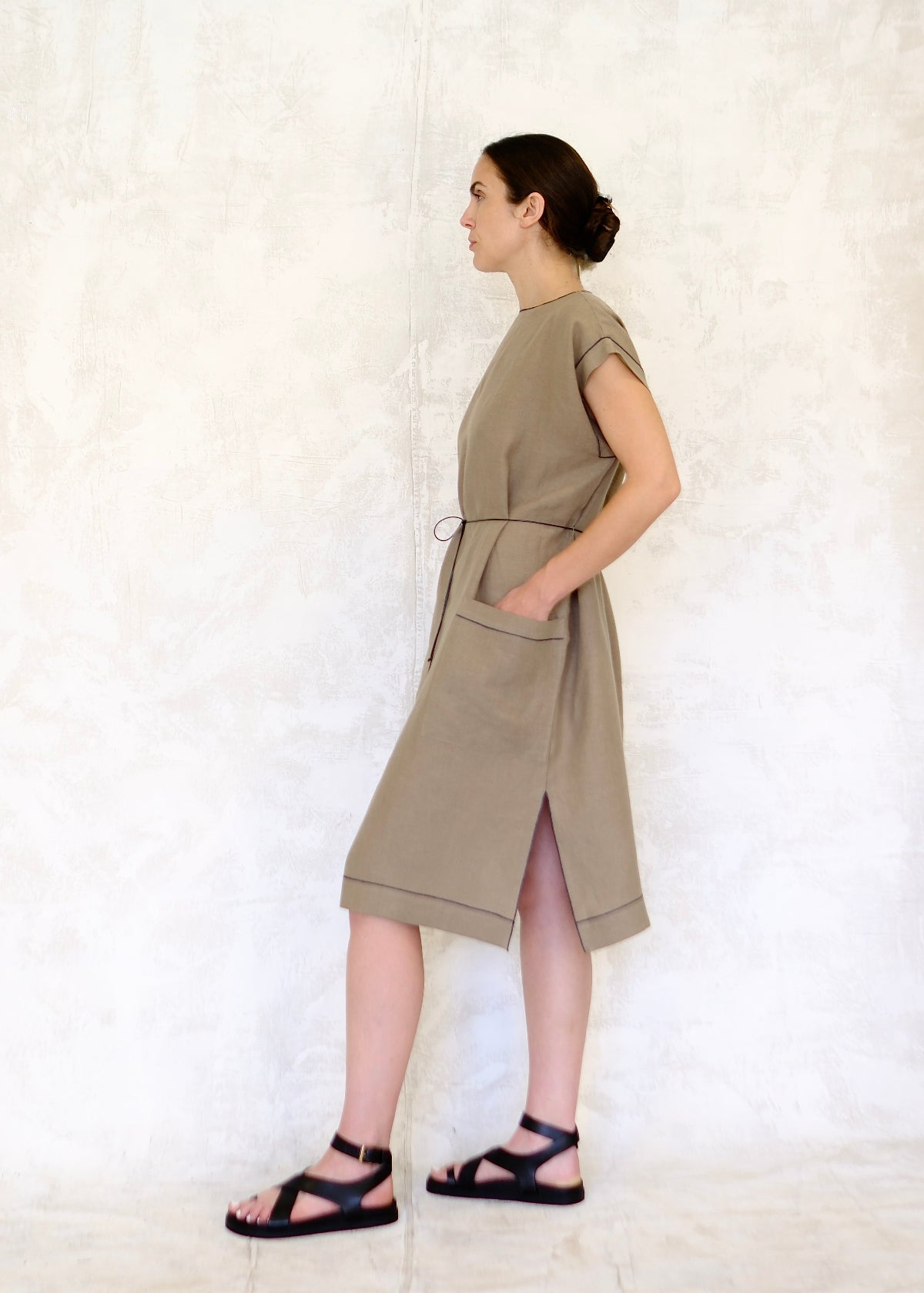 model in khaki colored linen sheath dress tied with cotton cord belt side view