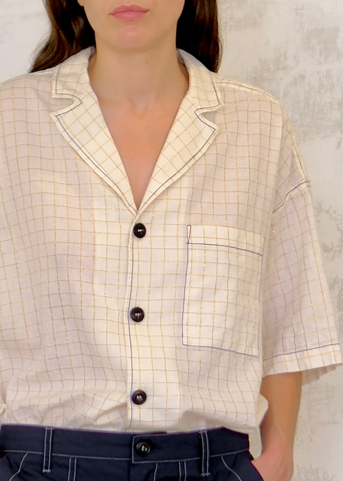 Beige checkered shirt with black buttons worn by a person against a neutral background