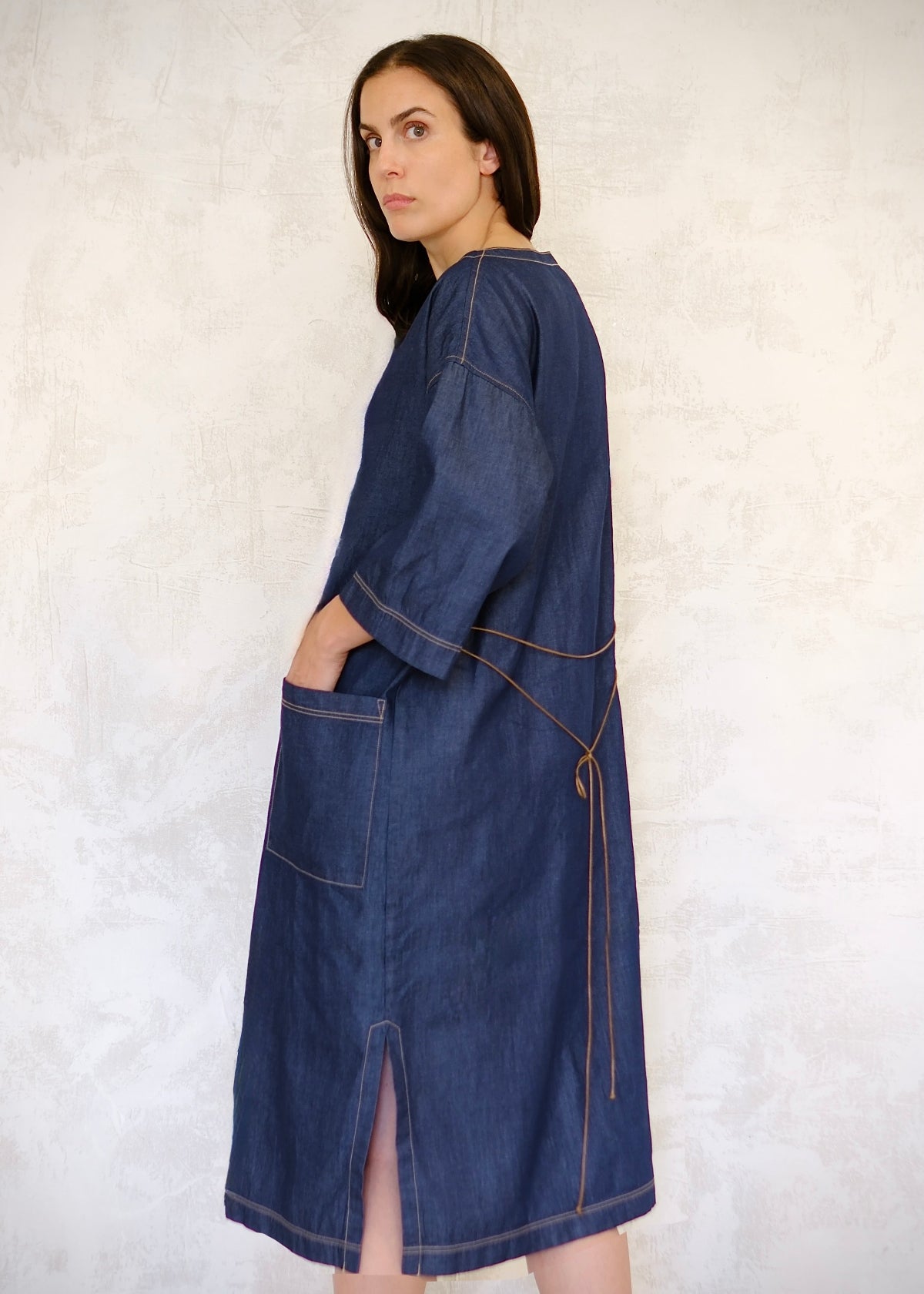 denim dress with cord belt tied in back and hand in pocket