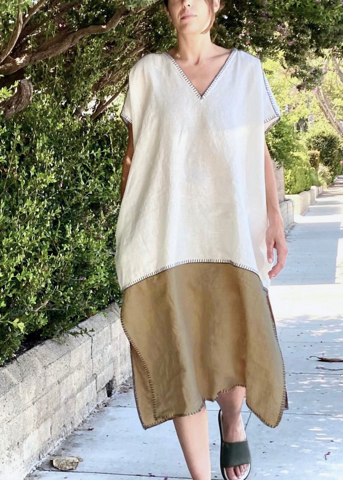 Woman wearing a white and olive dress standing against a plain wall.