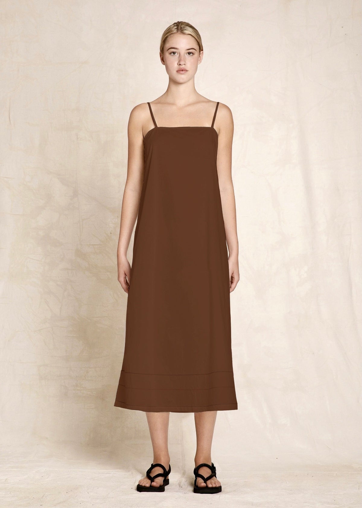 Woman wearing a brown slip dress against a plain background