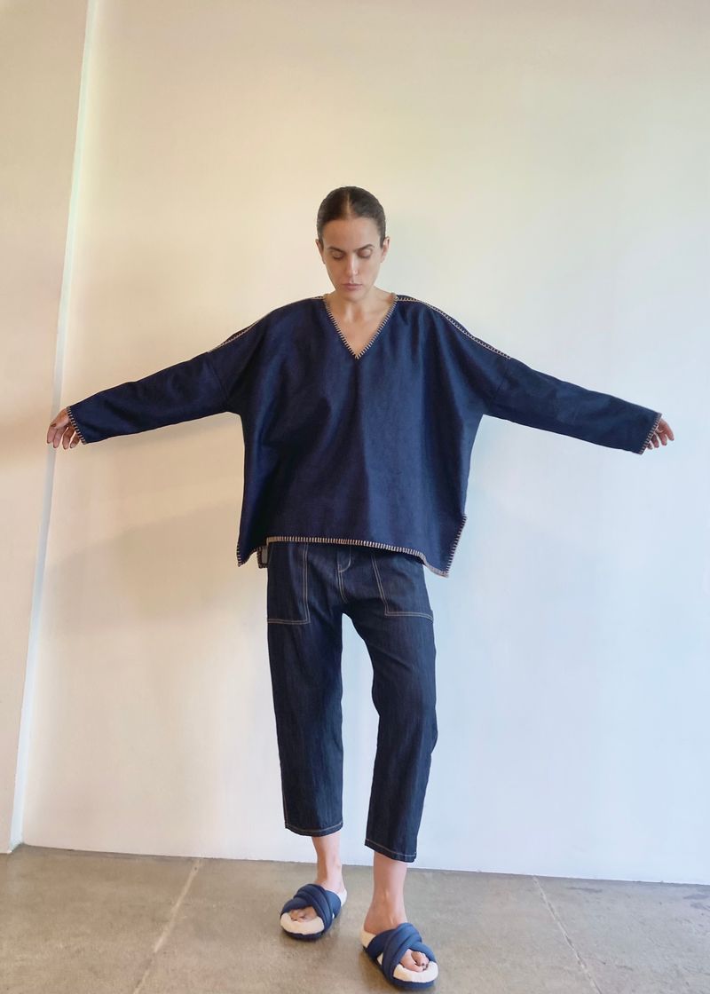 Person with arms outstretched wearing a navy blue denim poncho sh and jeans standing against a plain background