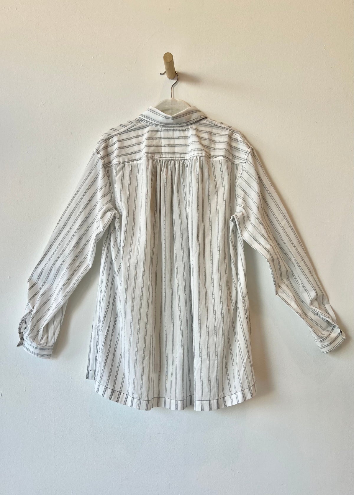 back of a white shirt with thin black stripes hanging against a white wall