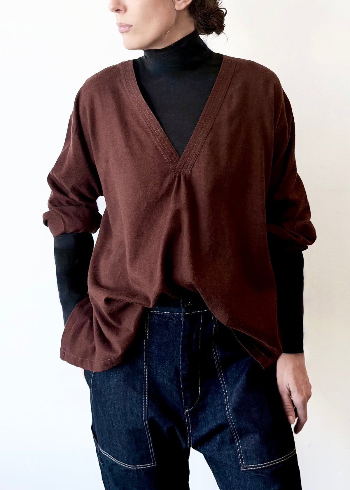Woman wearing a light gray Farmer's Smock with dark gray drawstring flannel pants against a plain background