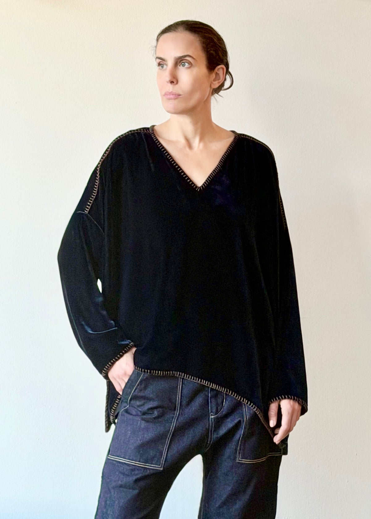 Model wearing a front tucked navy blue velvet Praia tunic with long sleeves and a V-neckline against a plain wall.