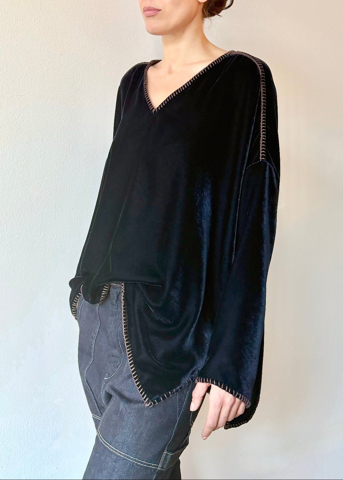 Model wearing a front tucked navy blue velvet Praia tunic with long sleeves and a V-neckline against a plain wall.
