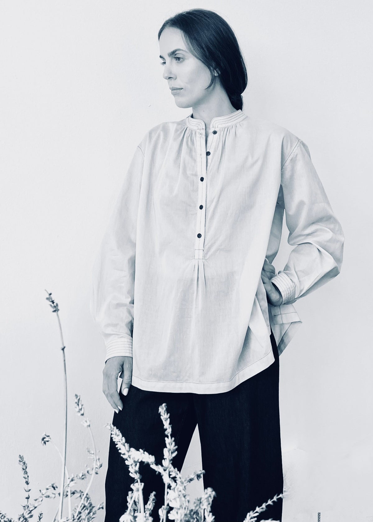 Woman wearing a light-colored blouse with black pants against a white background