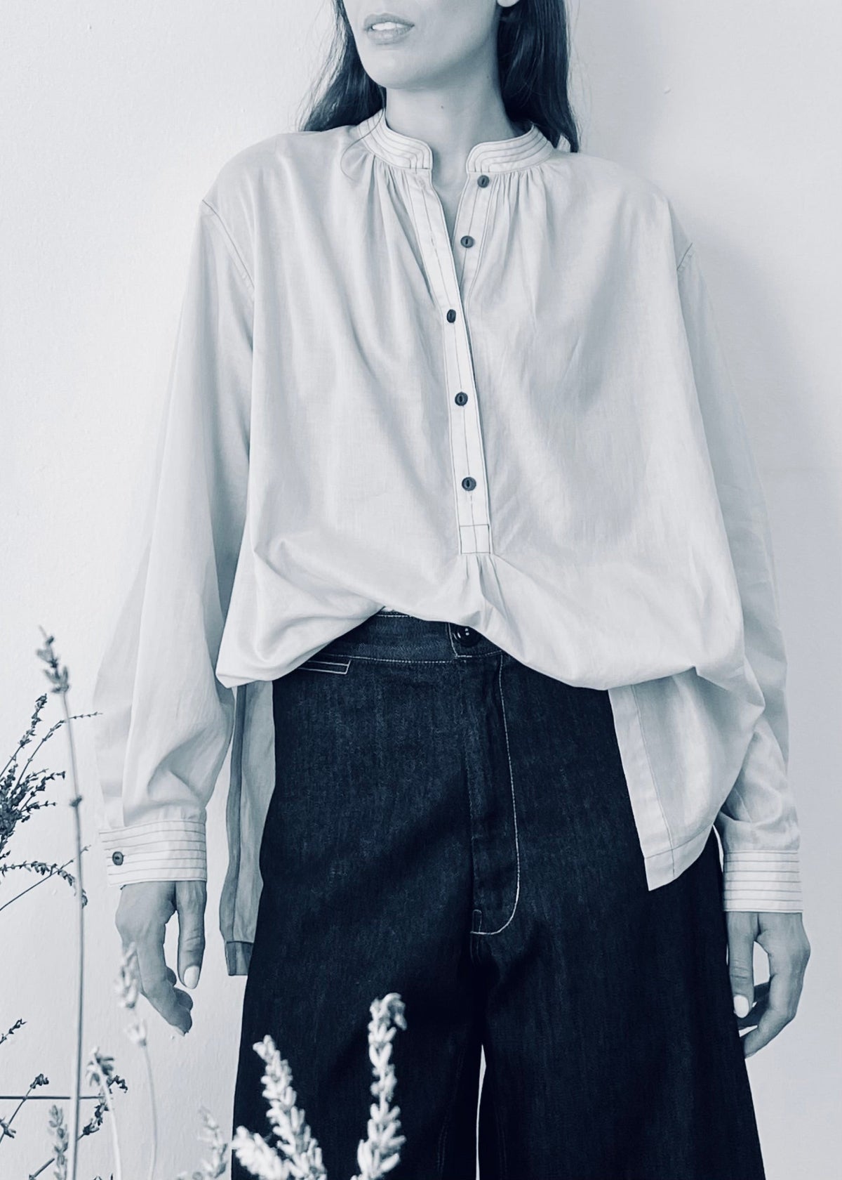 Person wearing a light-colored blouse tucked in and dark pants against a white background