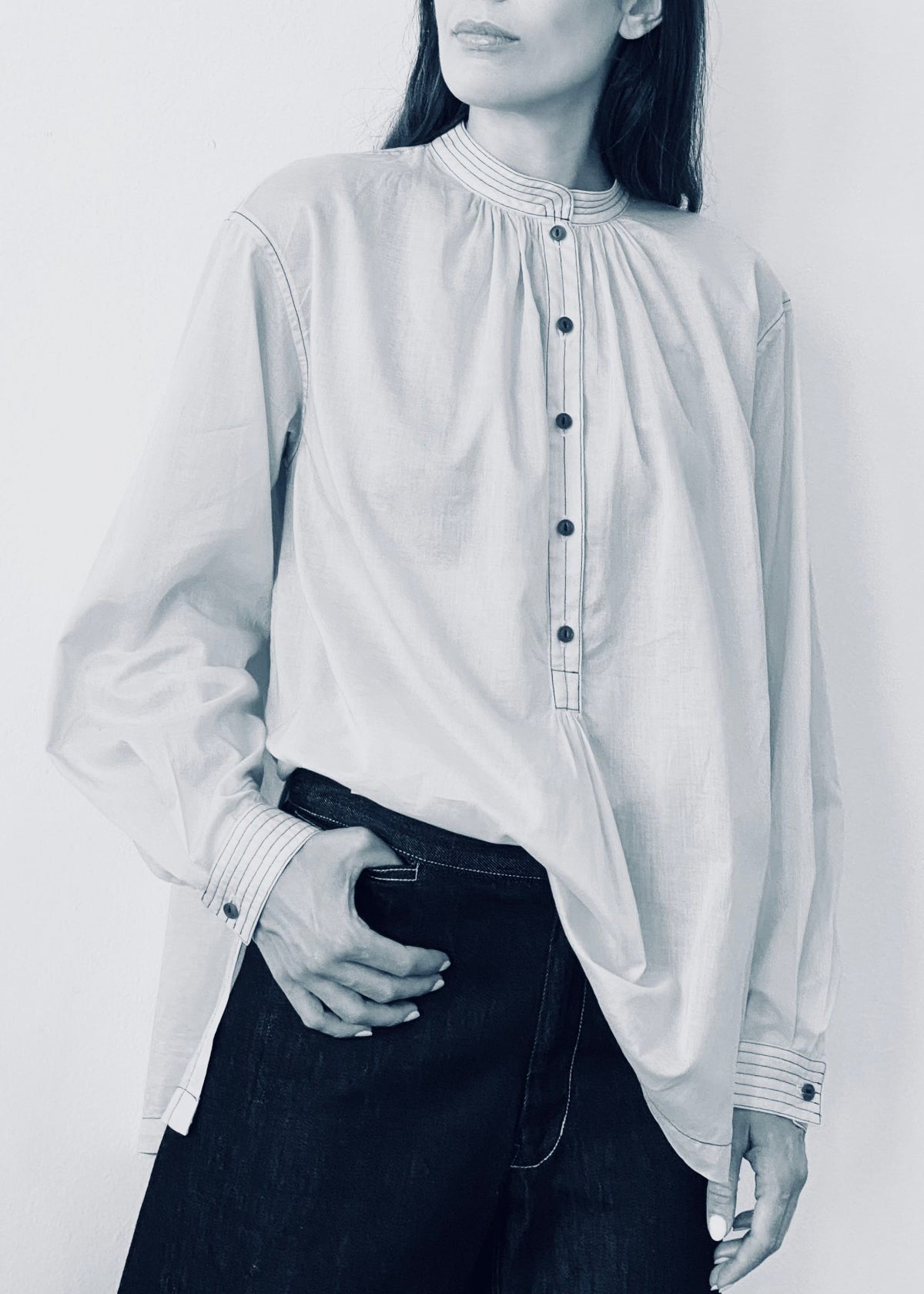 Person wearing a light-colored blouse with a high collar and long sleeves on a plain background