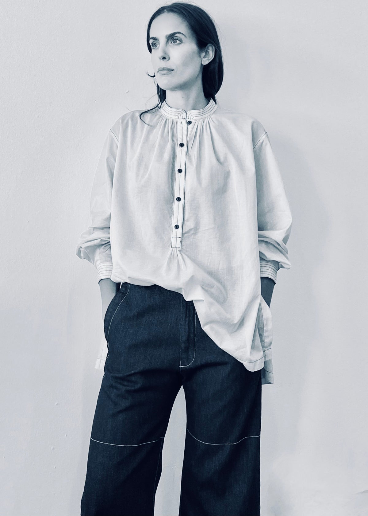 Person wearing a white blouse and dark pants against a plain background