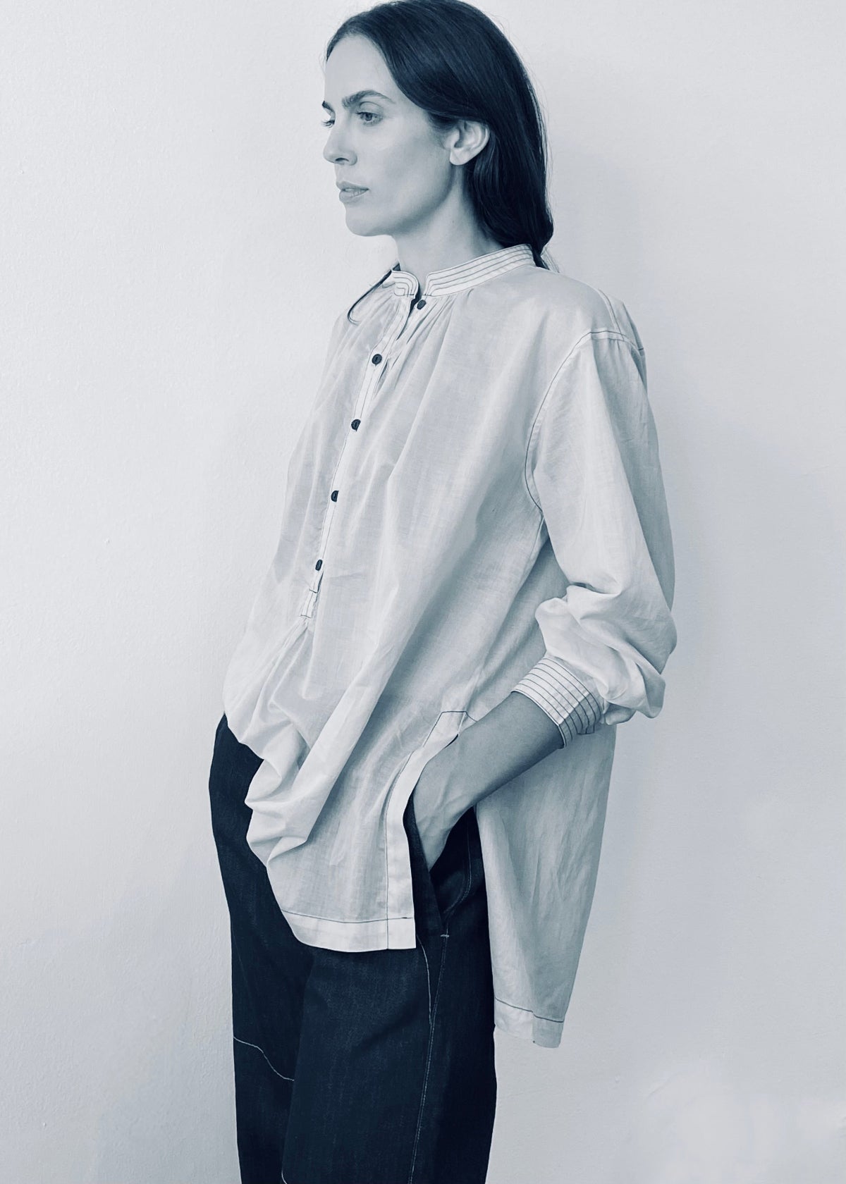Person wearing a light-colored shirt with rolled-up sleeves against a plain background