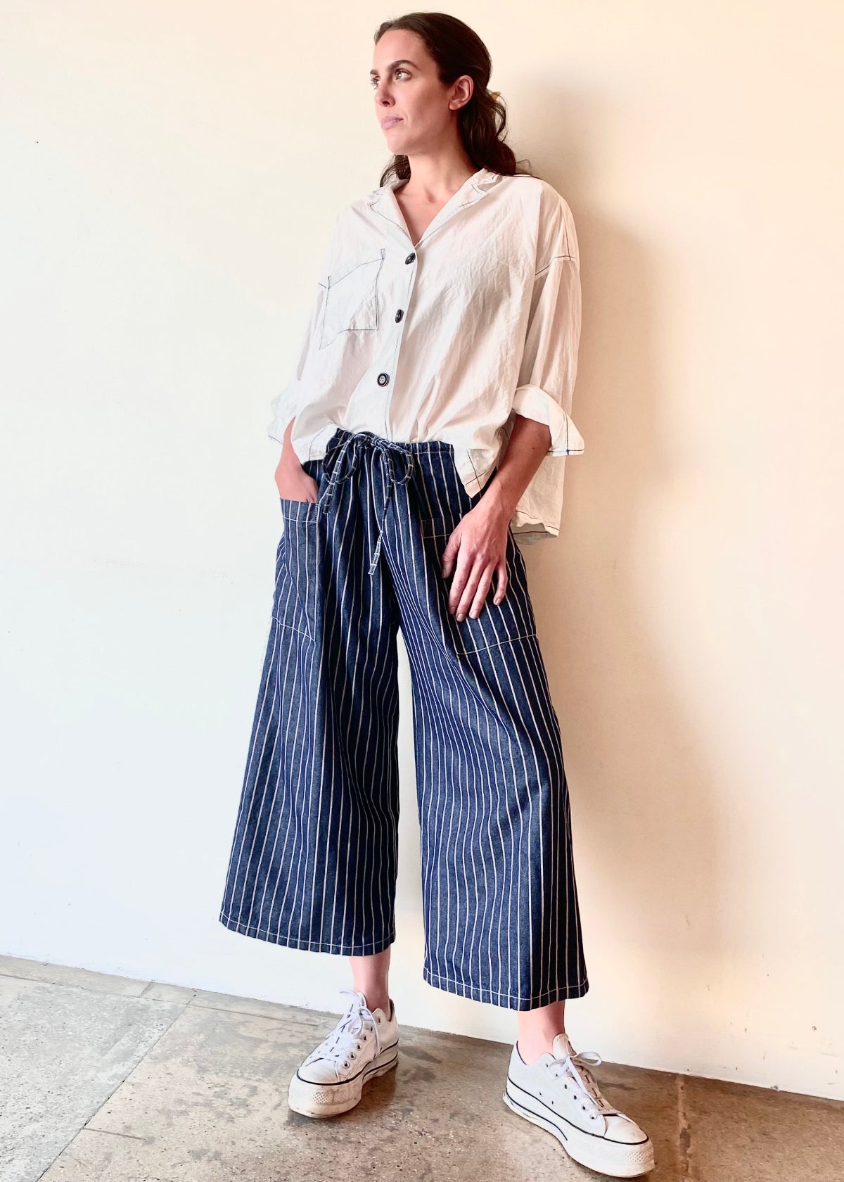 blue and white striped denim cropped drawstring pants with white button down top. Hand in pocket
