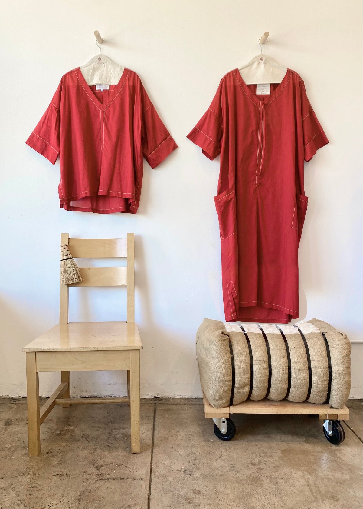 Two red garments hanging on hangers against a white wall
