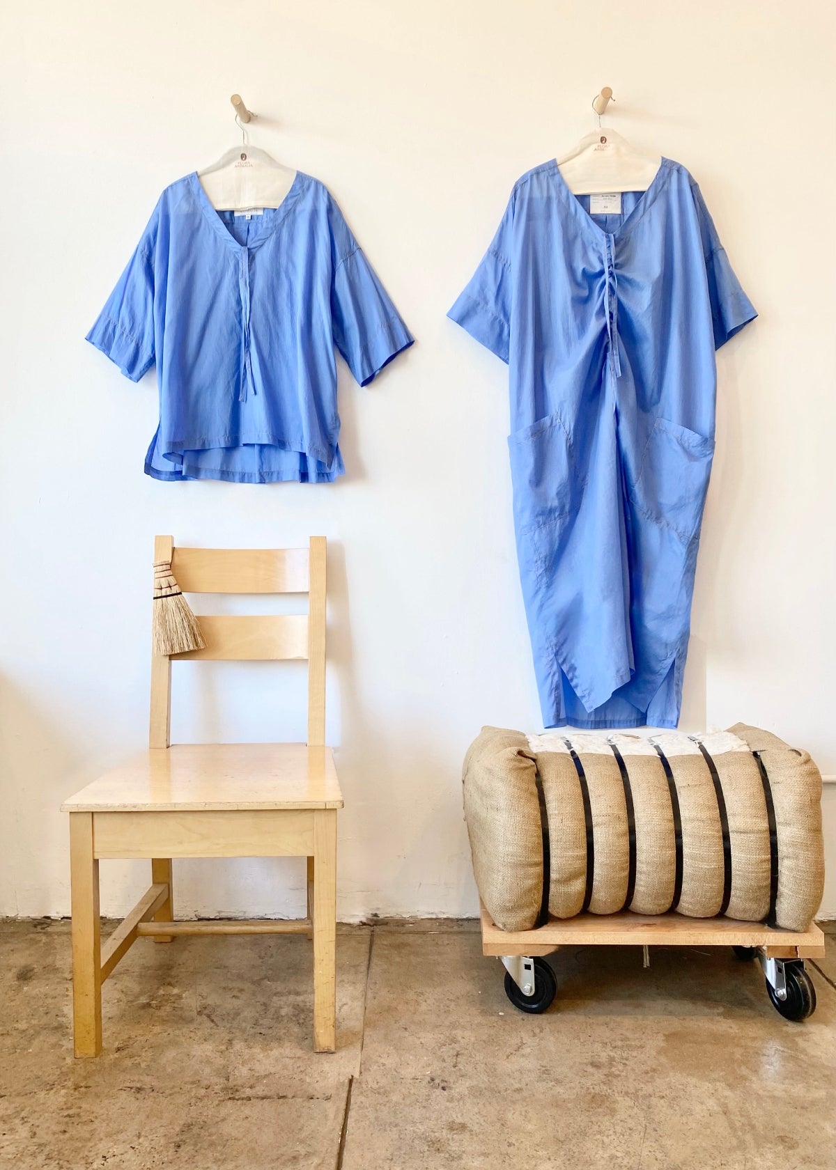 Two blue garments hanging on hangers against a white wall