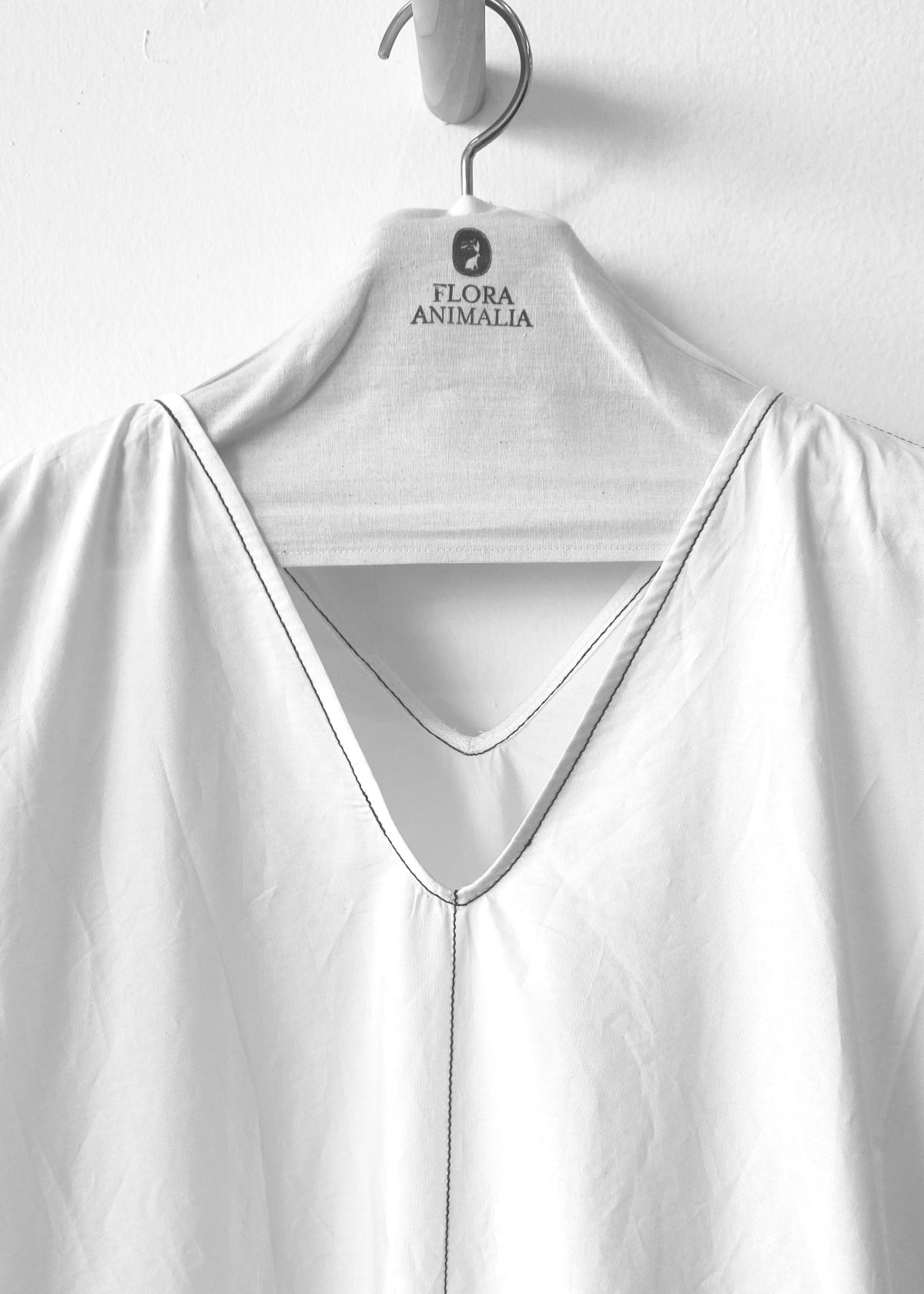 White v neck detail on a hanger with 'Flora Animalia' branding against a white background