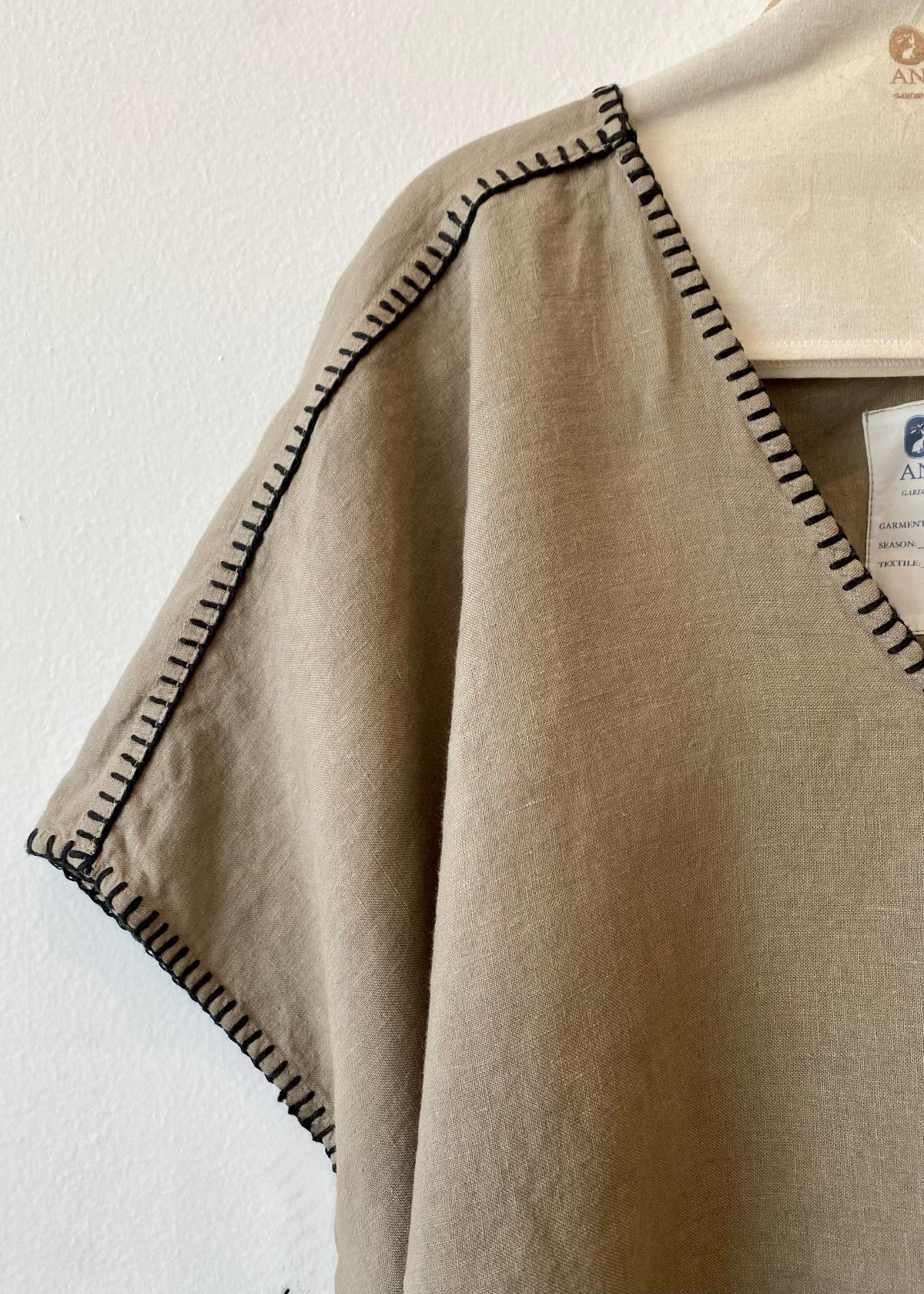 close up Beige v-neck shirt with black trim on a white background