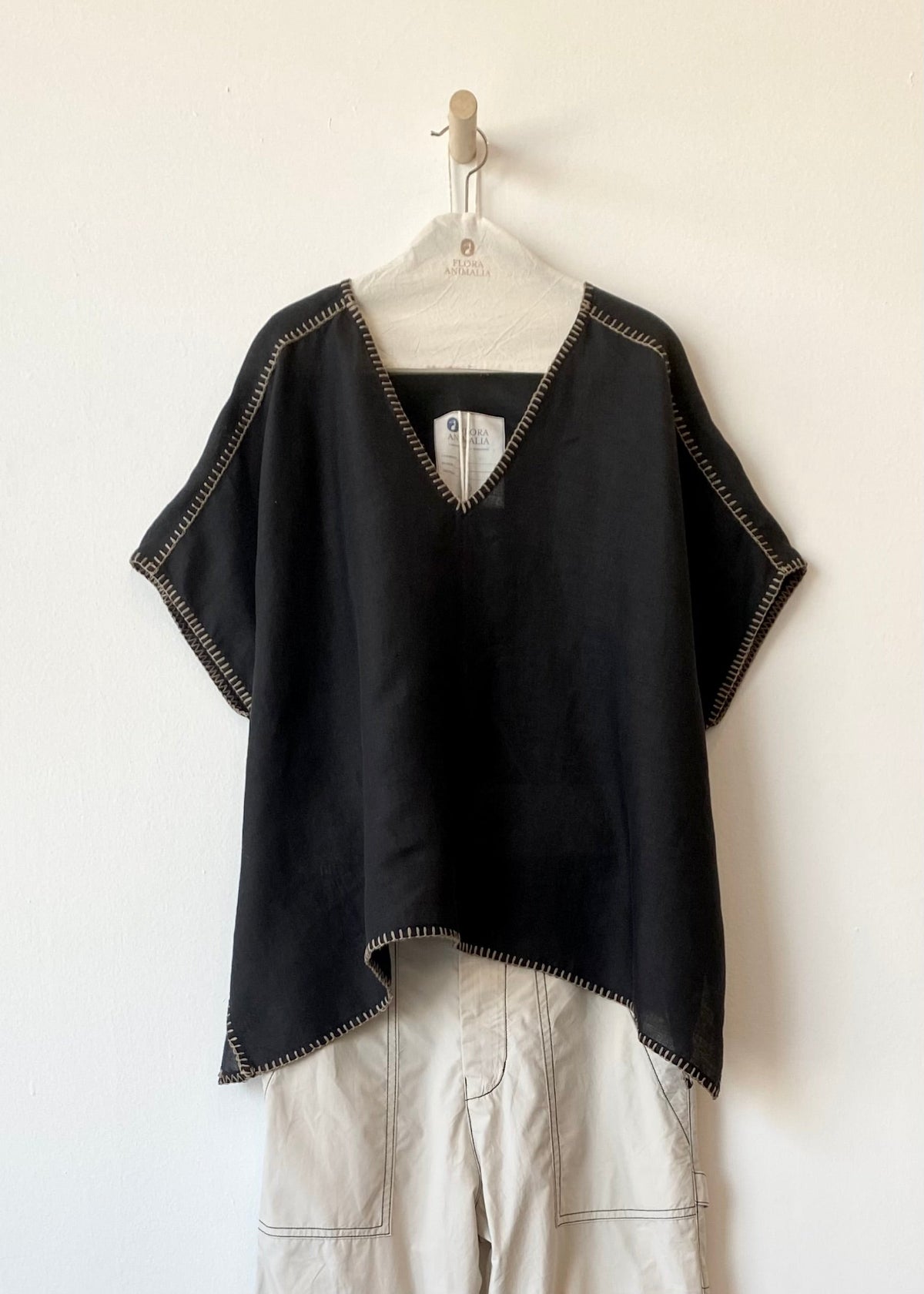 black tunic with tan edge stitching hanging on a white wall