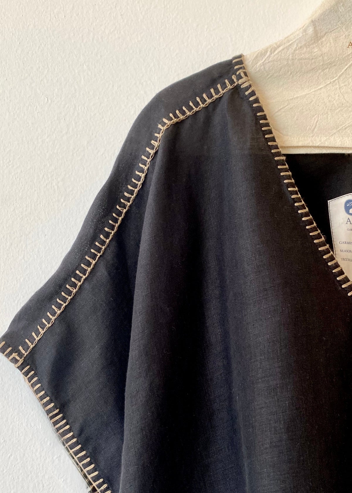 black linen garment with tan stitching on a white background