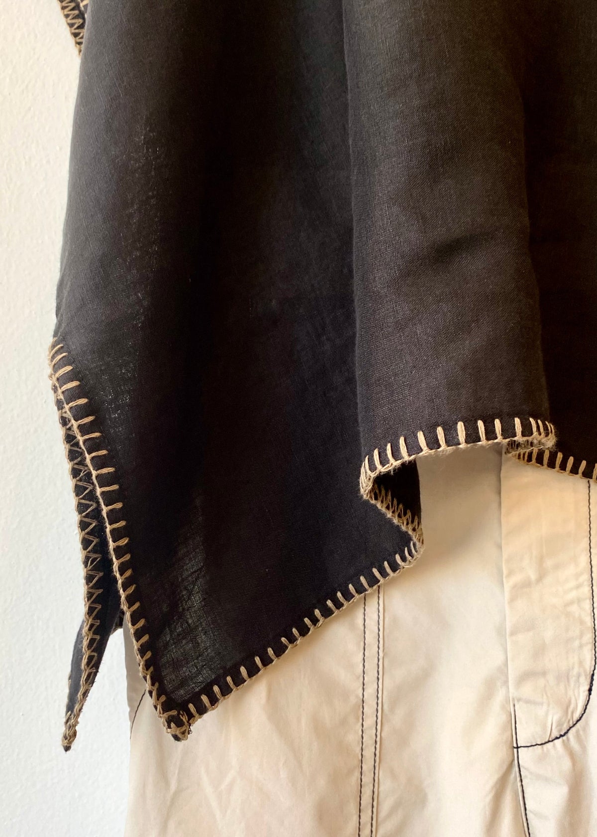 black shirt hem draped over a light-colored garment with visible tan stitching.