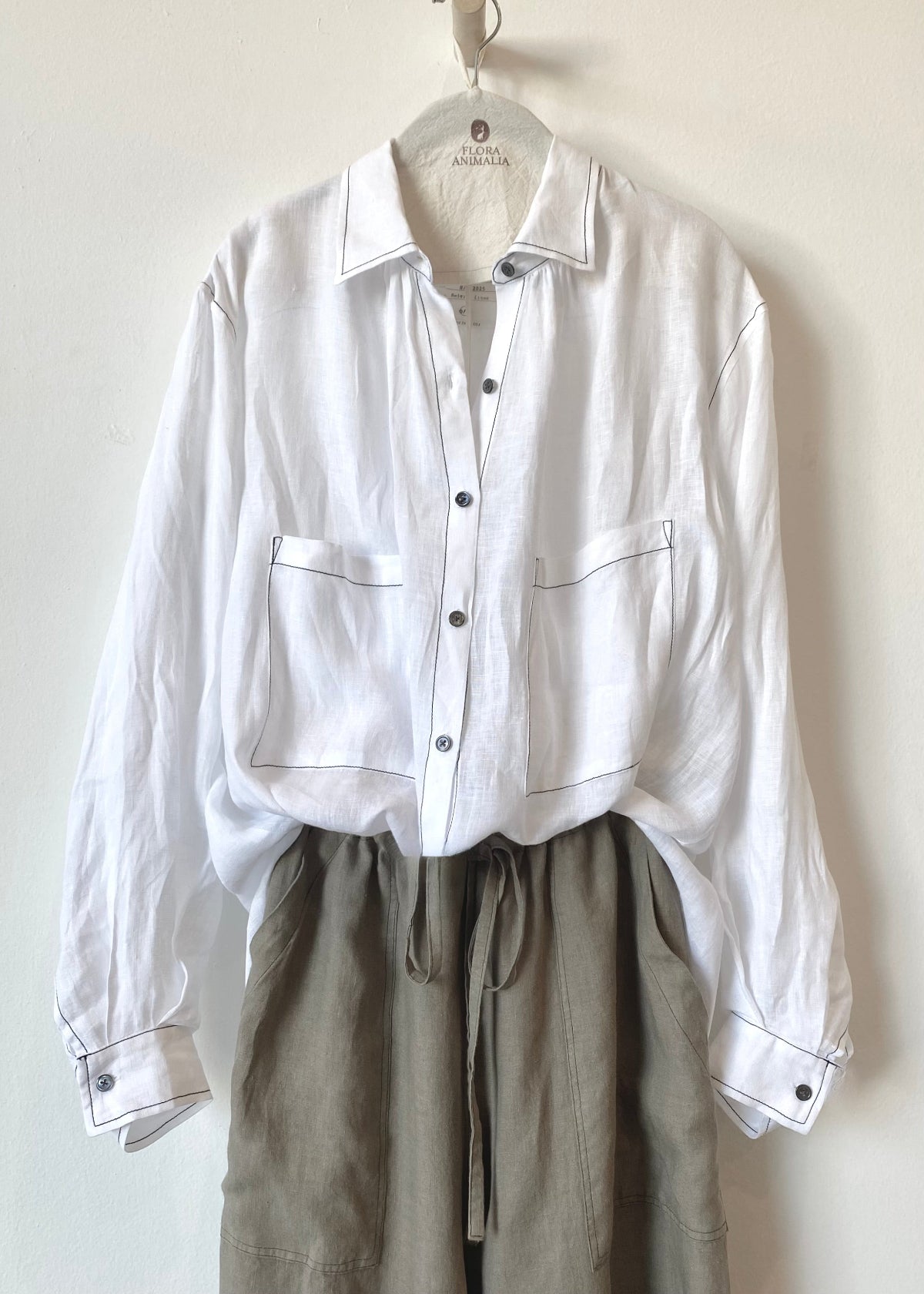 White shirt with long sleeves buttoned at cuffs and gray pants on a hanger against a white background