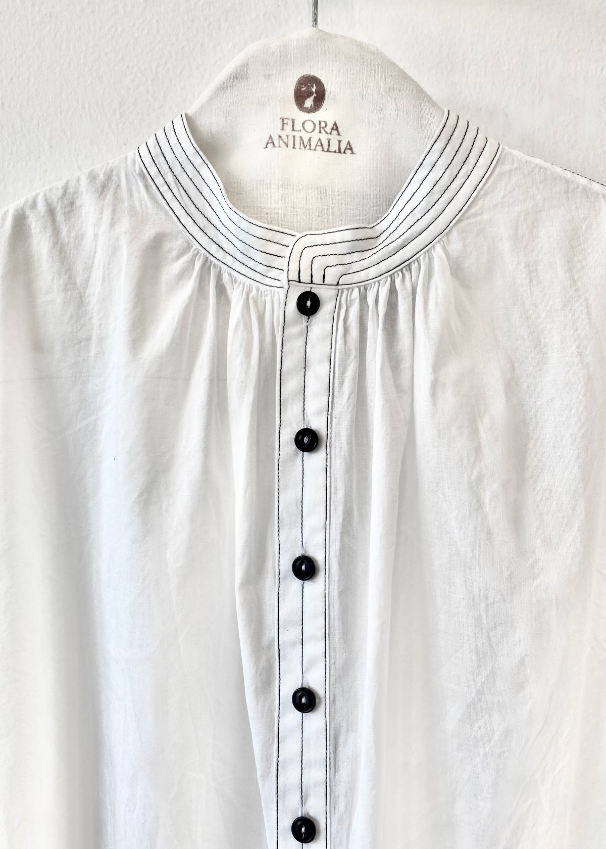 close up of White shirt with black buttons on a hanger with 'Flora Animalia' label.