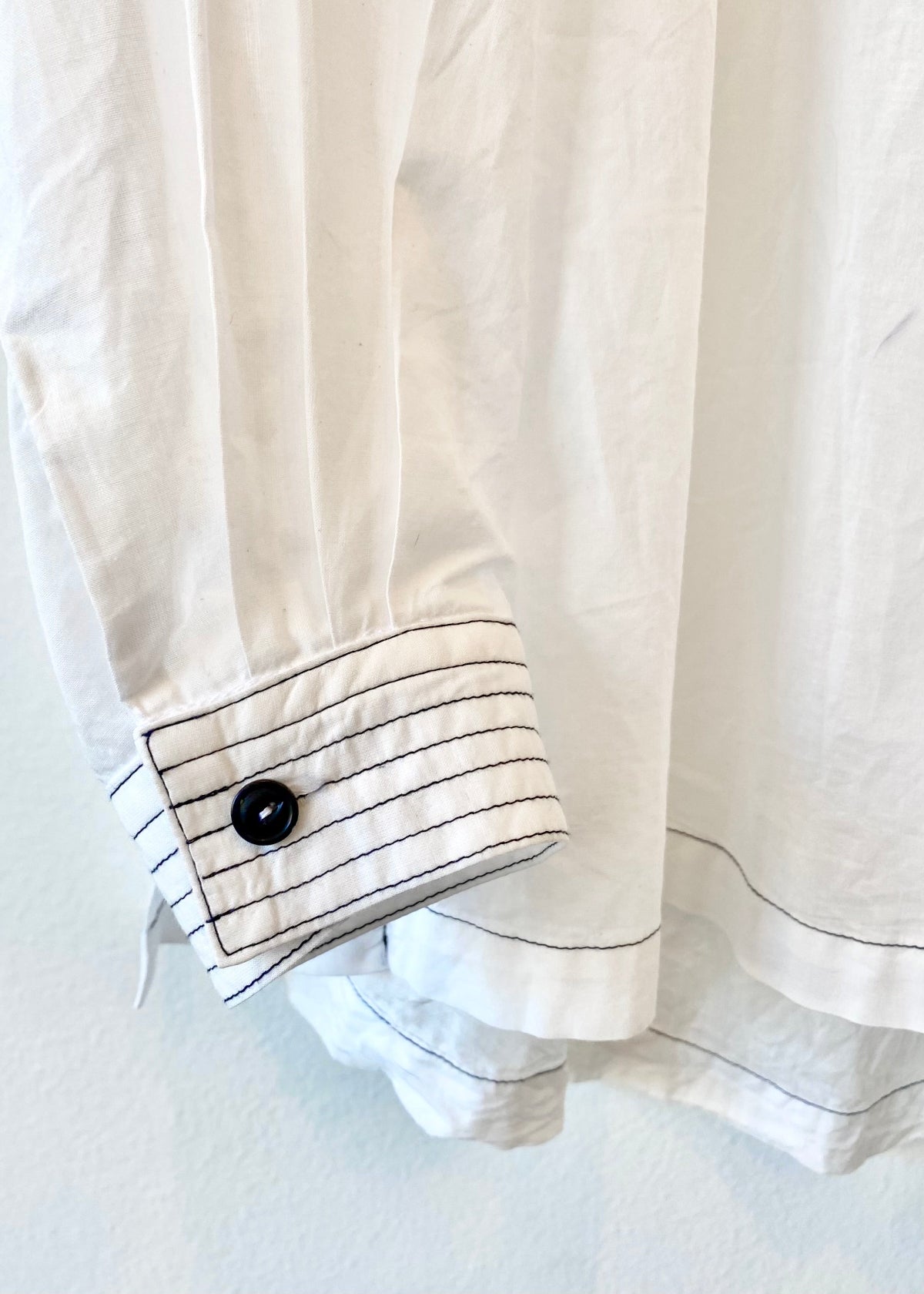 Close-up of a white shirt cuff with black buttons and trim on a light background