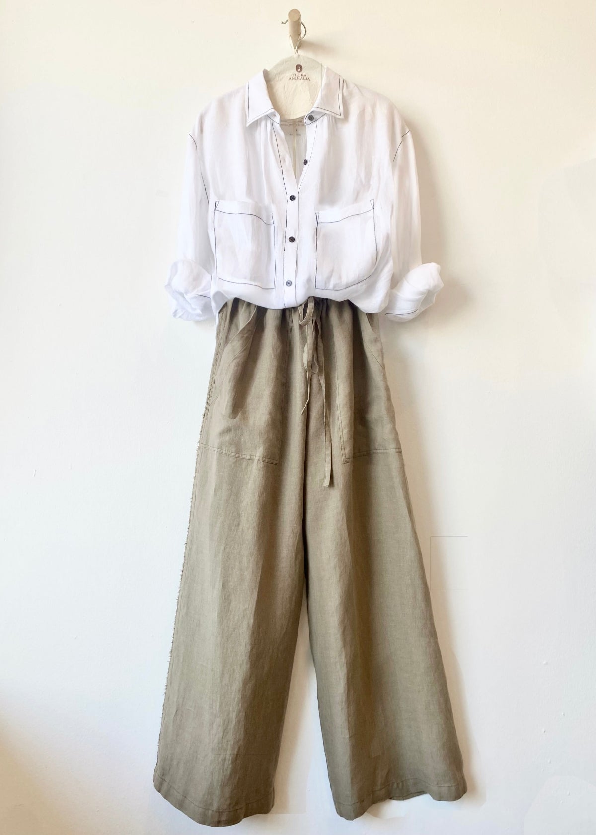 White shirt and beige wide-leg pants on a hanger against a white background