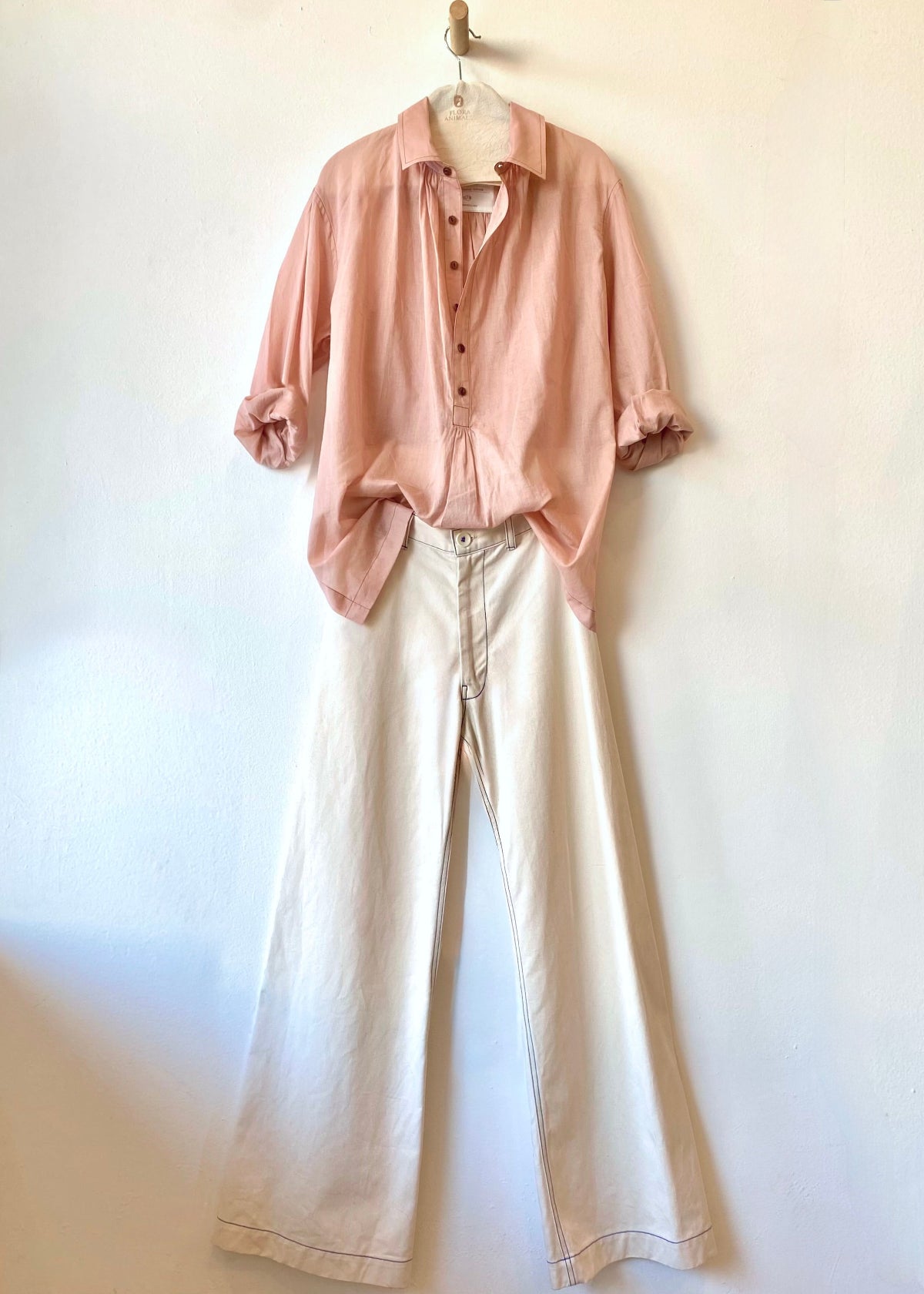 Pink shirt and beige pants hanging on a white wall