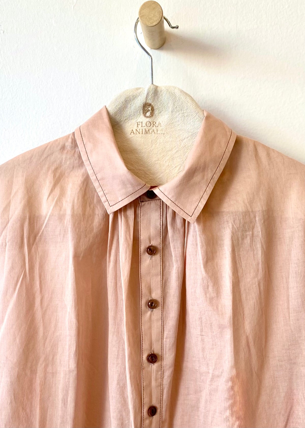 Pink shirt collar and buttons on a hanger with 'Flora Animal' label against a white background