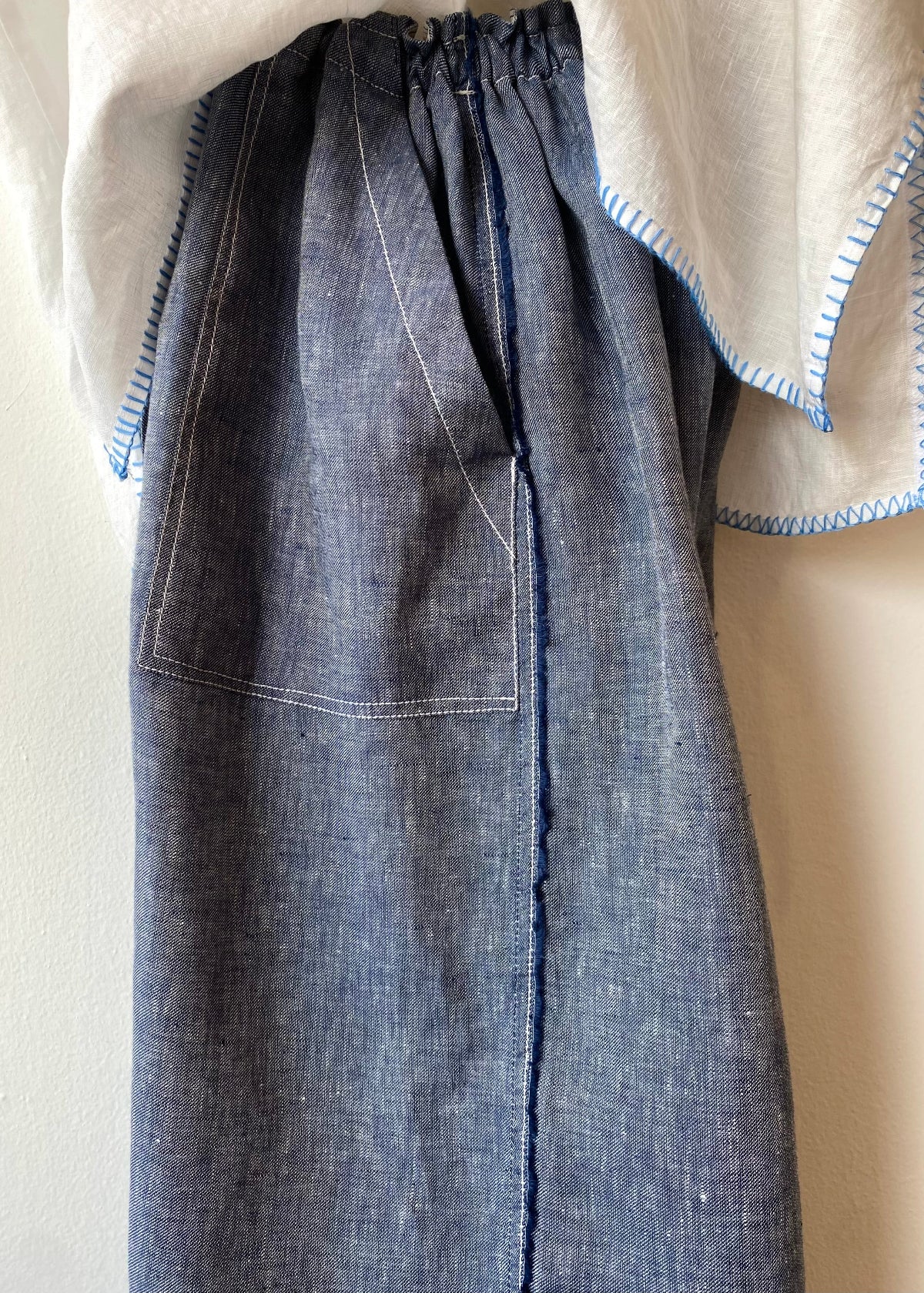 side tight image of Blue linen pants worn over a beige shirt on a neutral background