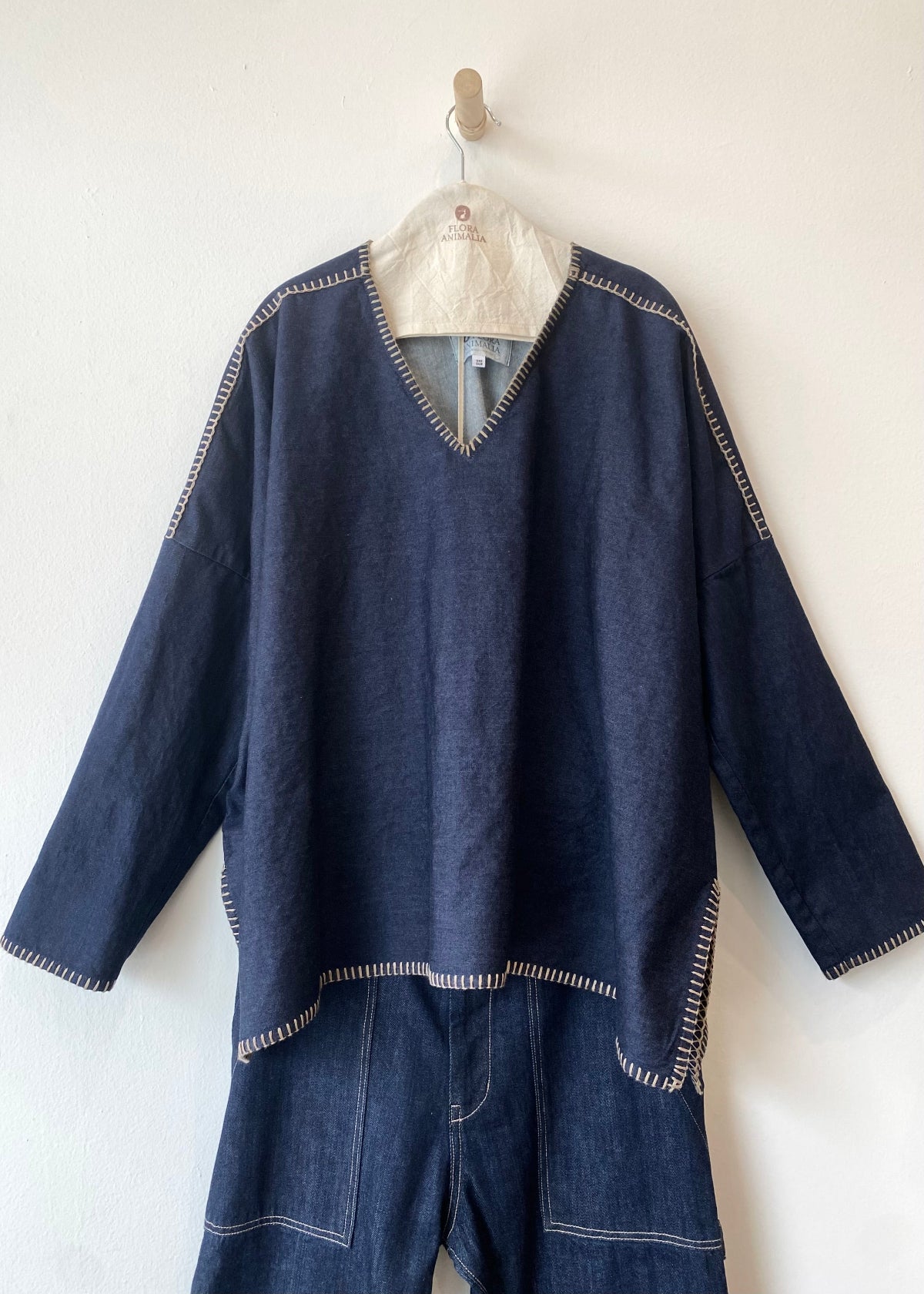 Person with arms outstretched wearing a navy blue denim poncho sh and jeans standing against a plain background