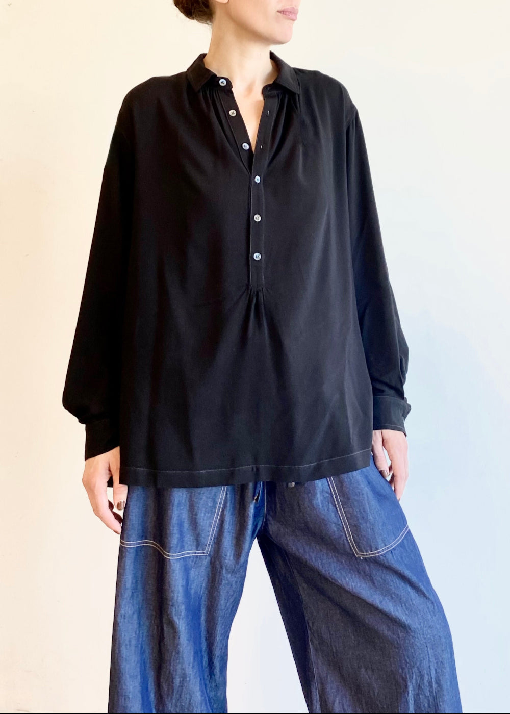Person wearing a black button Agnes shirt and drawstring blue jeans against a plain background