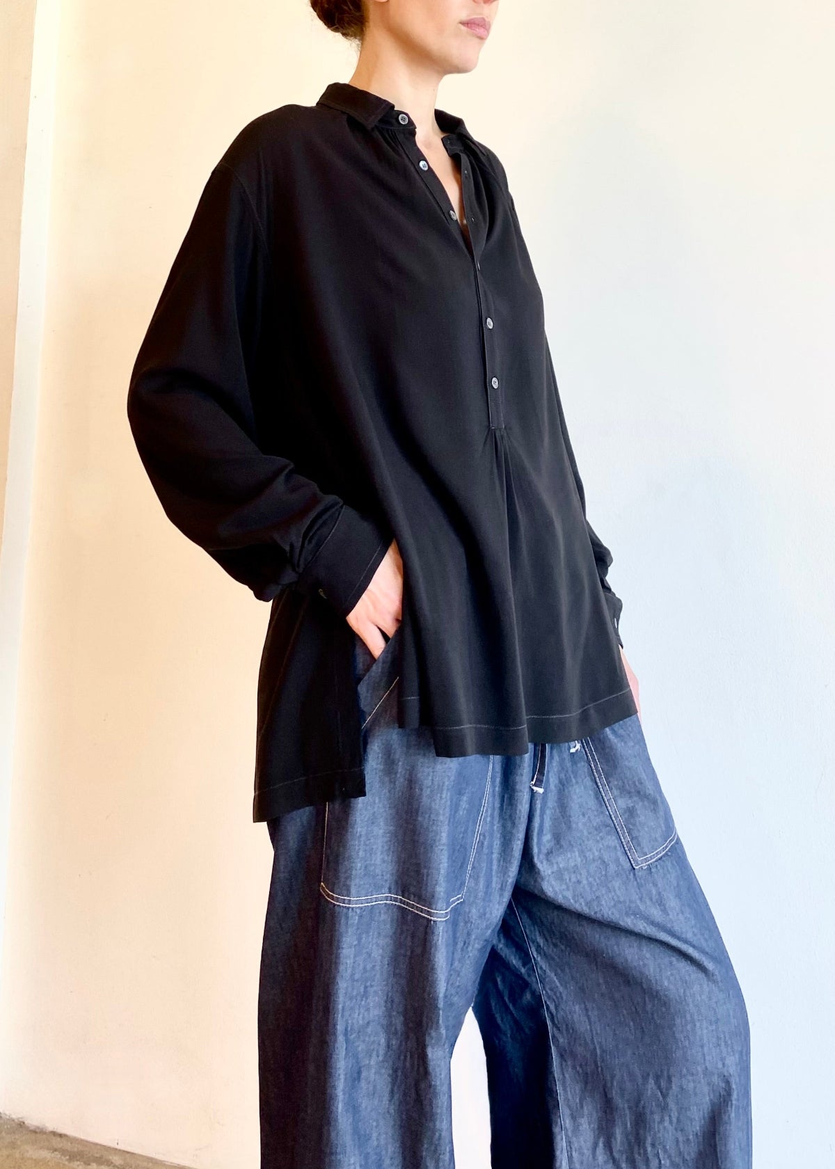 Person wearing a black button Agnes shirt and drawstring blue jeans against a plain background