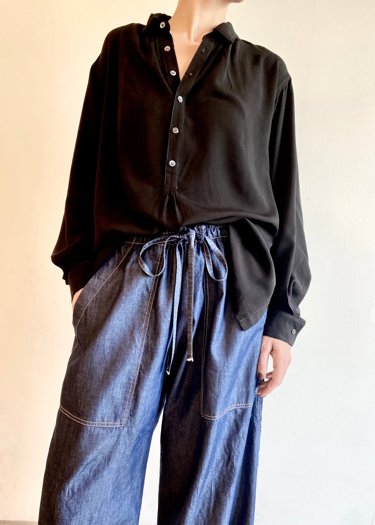 Person wearing a black button Agnes shirt and drawstring blue denim jeans against a plain background