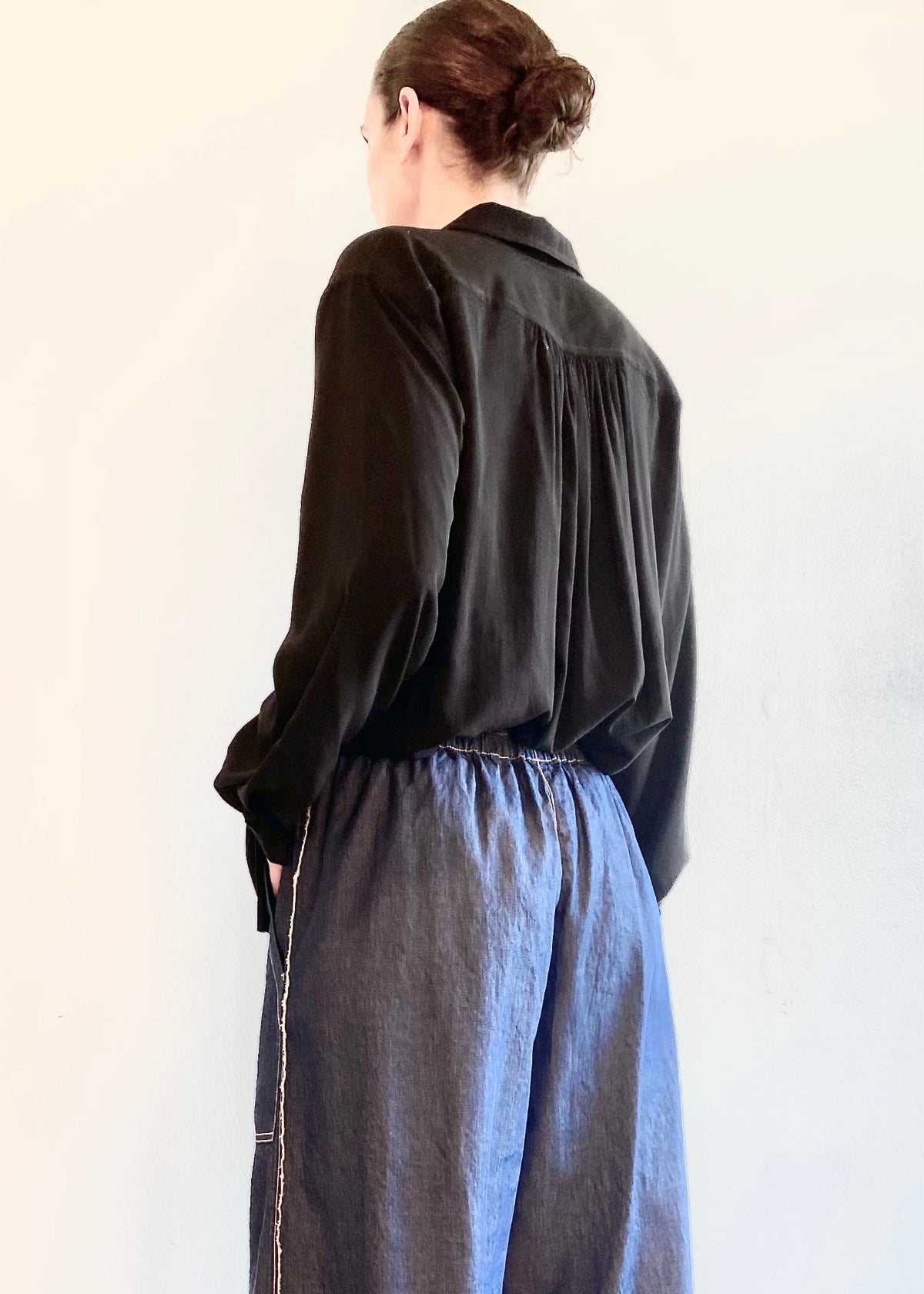 rear view of Person wearing a dark shirt and blue denim picker's  pants against a white background