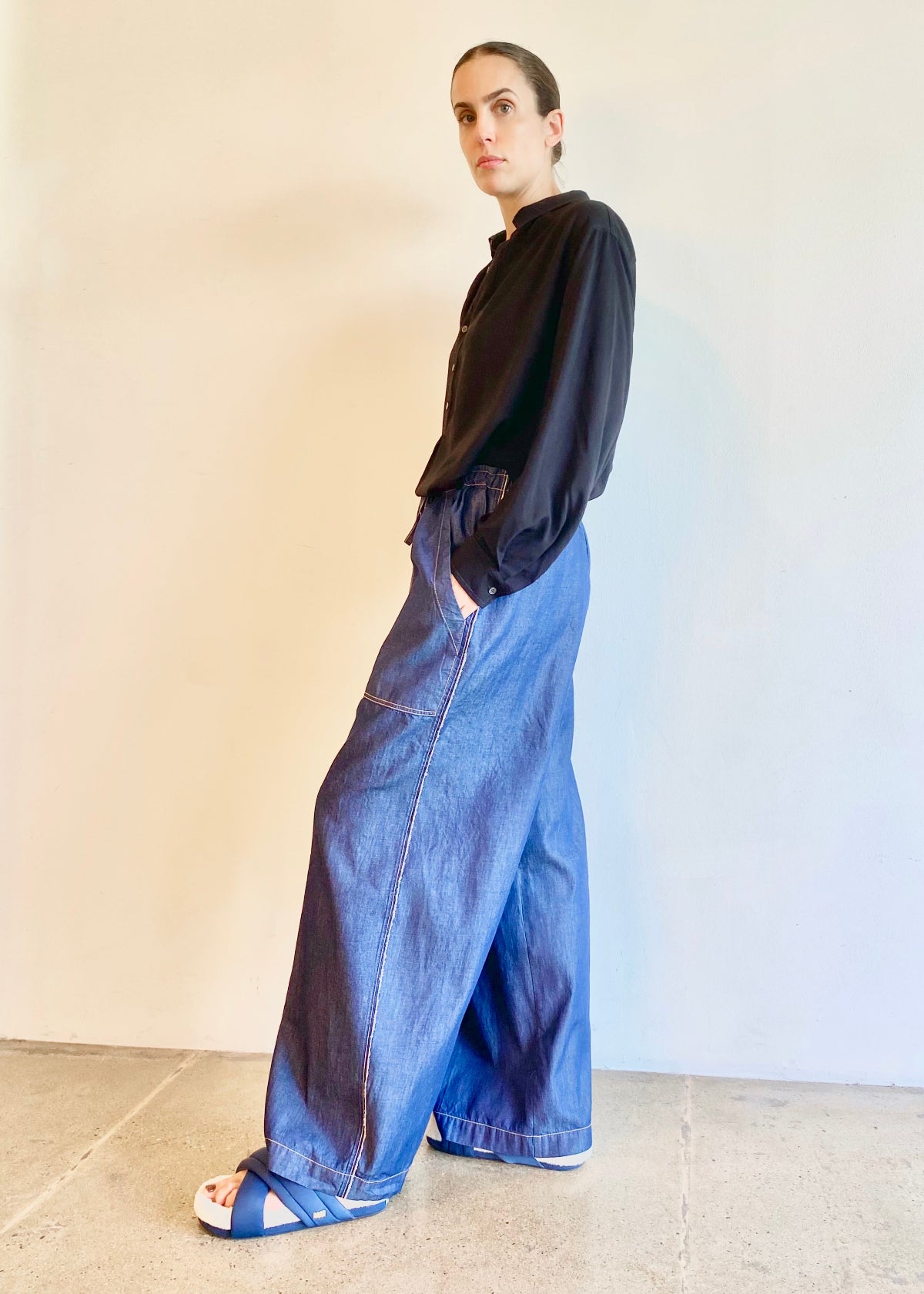 Person wearing a black button Agnes shirt tucked into drawstring blue jeans against a plain background