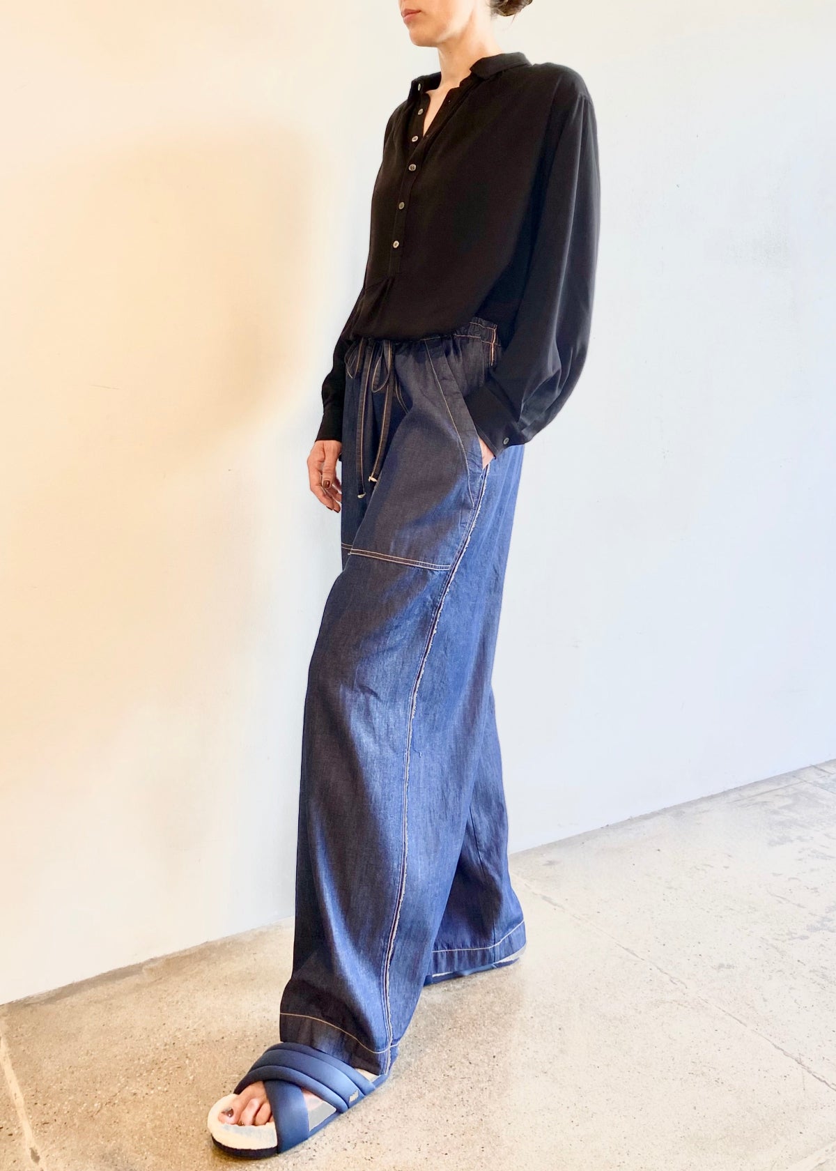 Person wearing a black button Agnes shirt tucked into drawstring denim blue jeans against a plain background