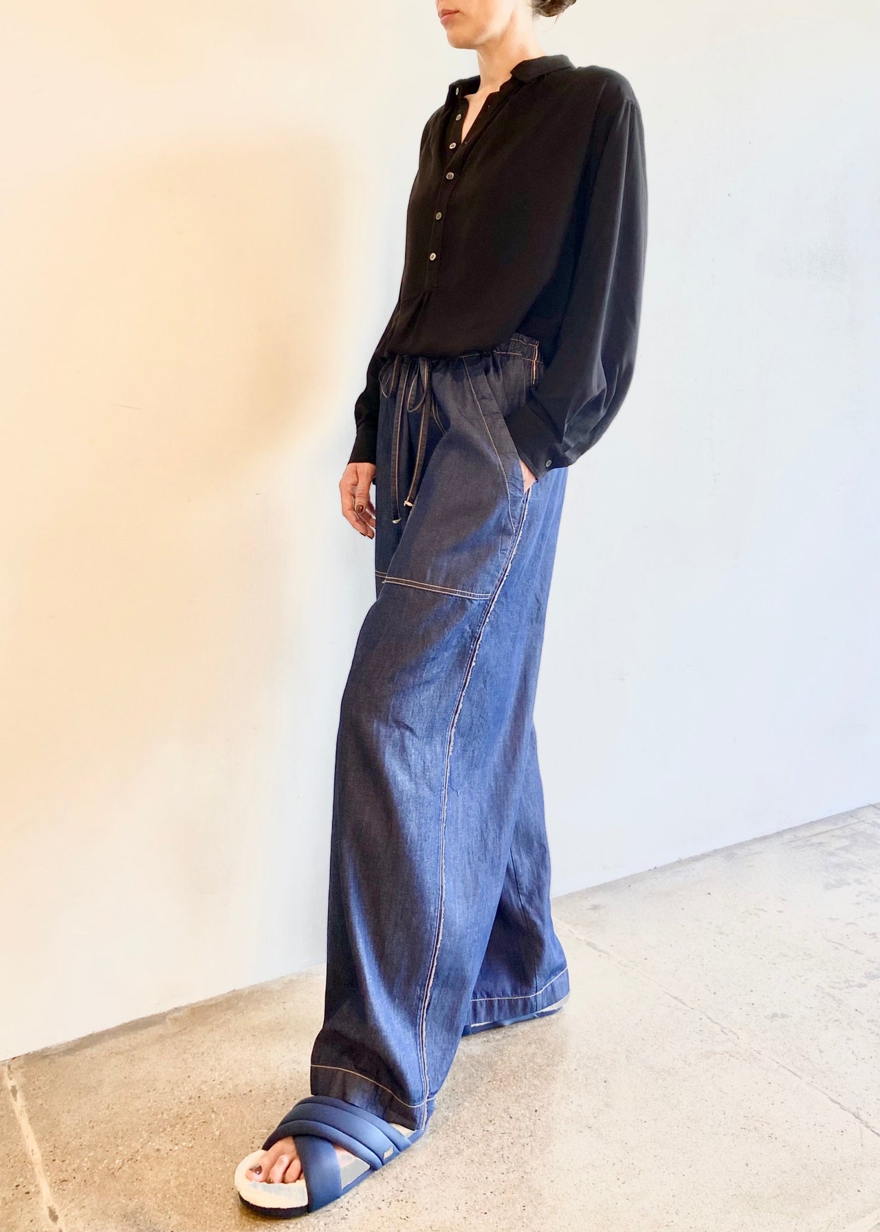 Woman wearing a beige Agnes blouse and blue wide-leg denim pants against a plain background