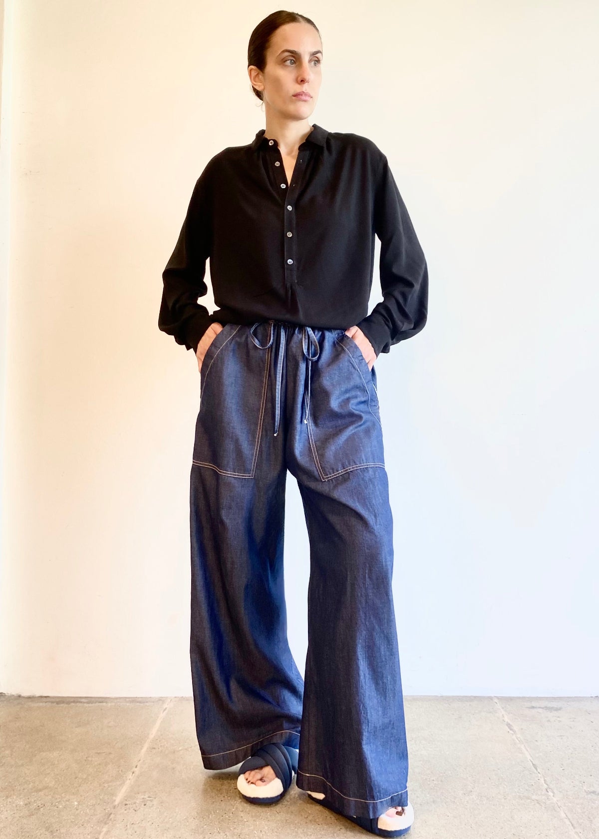 Person wearing a black button Agnes shirt tucked into drawstring denim blue jeans against a plain background