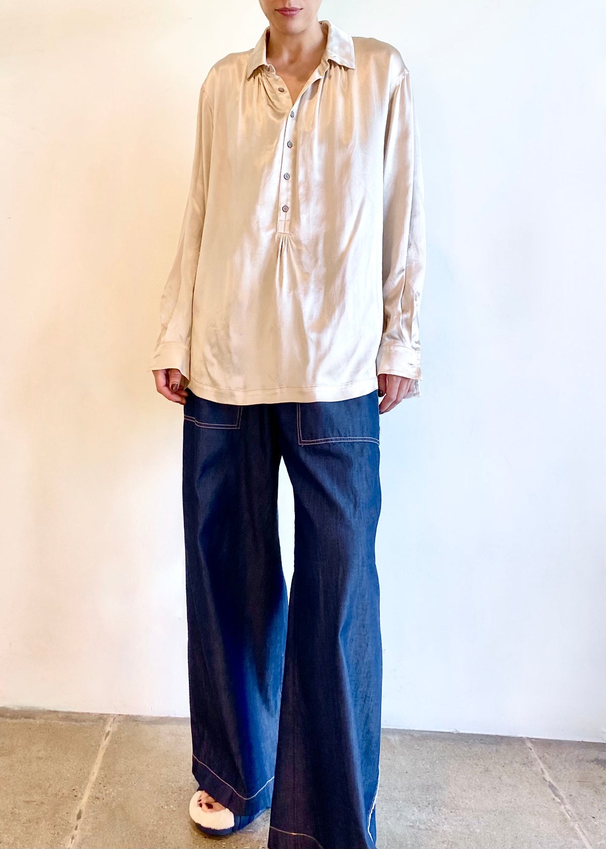Person wearing a beige collared shirt and blue jeans against a plain background