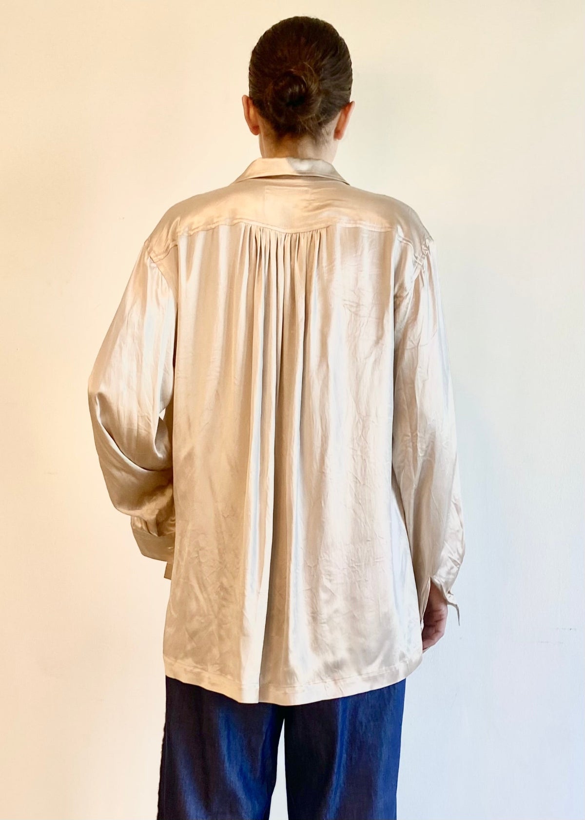 Rear view of person wearing a beige long-sleeve shirt with pleated yoke against a plain background